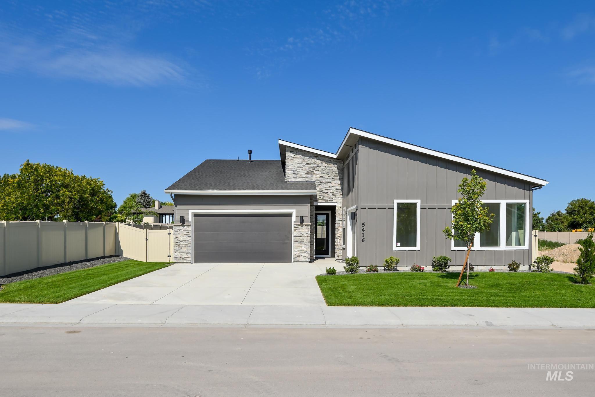 View of front of house with a gate, stone siding, an attached garage, and driveway