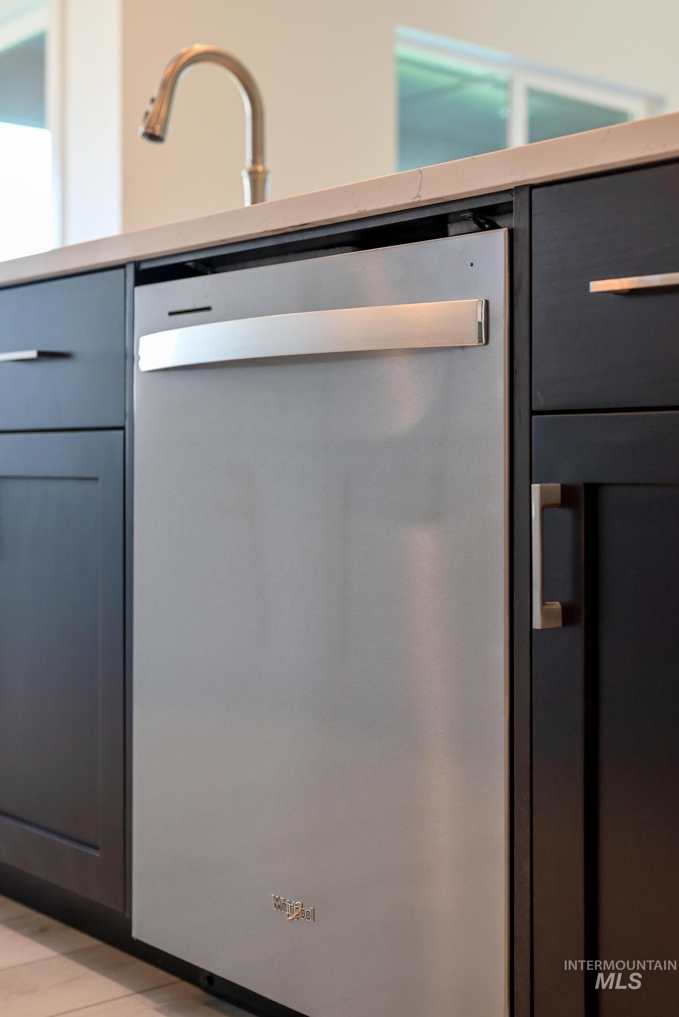 Kitchen view of stainless steel dishwasher, light countertops, and light wood-style flooring