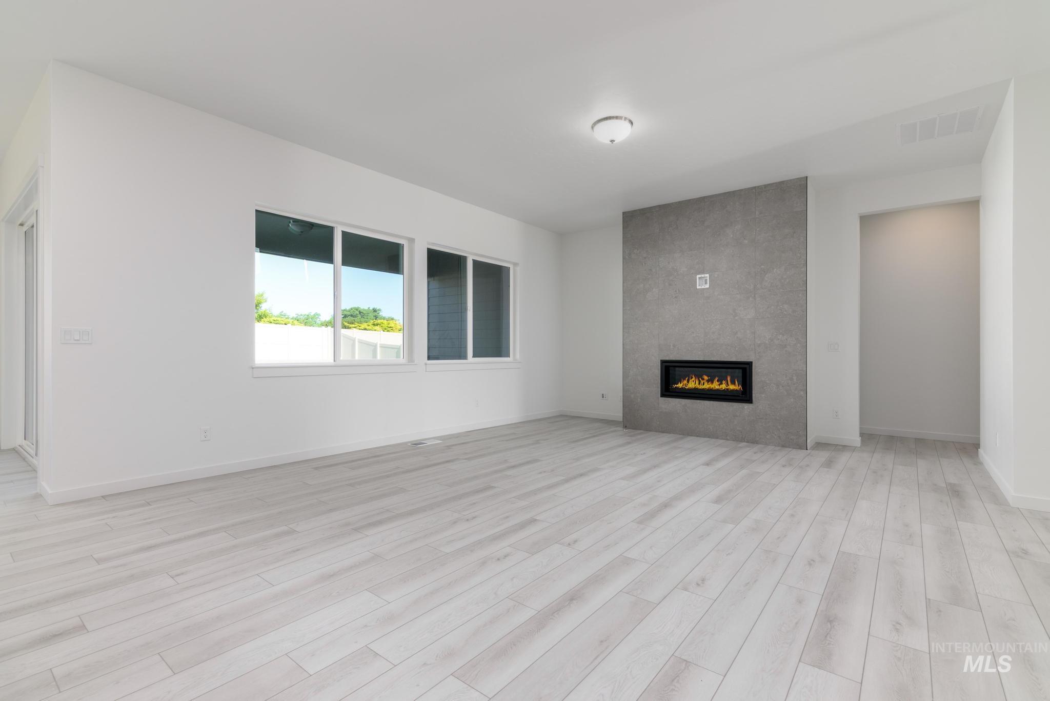 Unfurnished living room with a tiled fireplace and light wood-style flooring