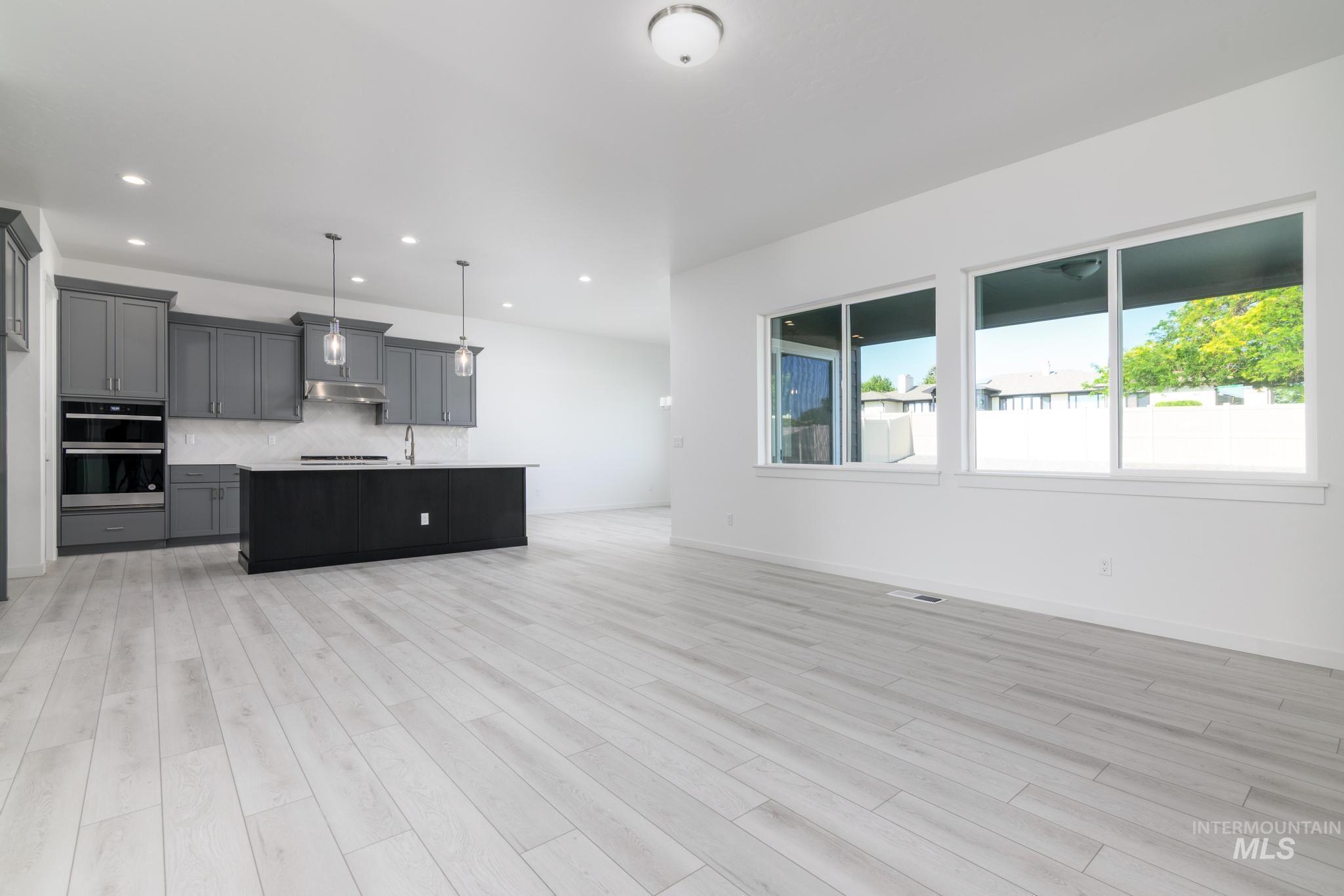 Kitchen with open floor plan, tasteful backsplash, an island with sink, hanging light fixtures, and light wood-style floors