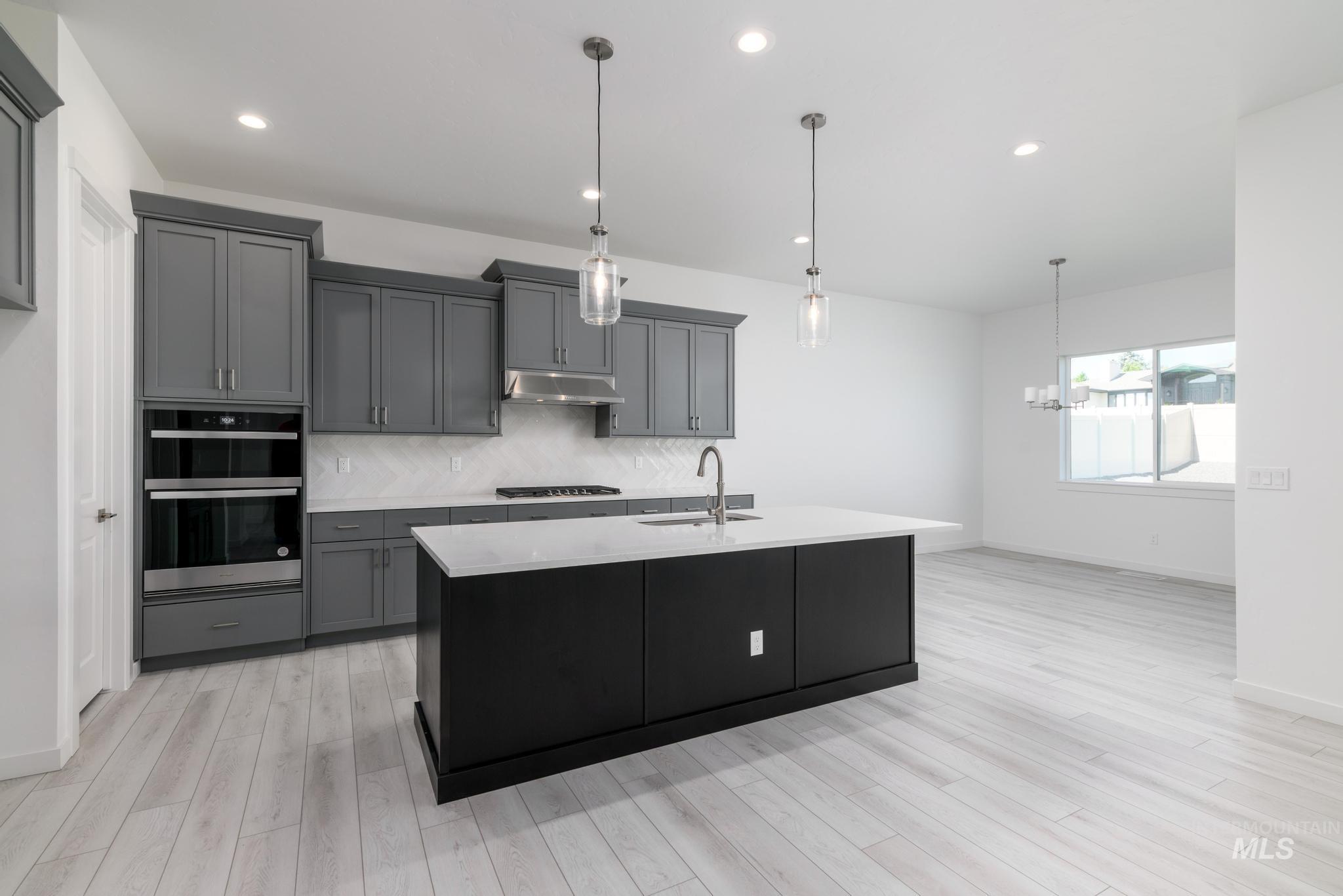 Kitchen featuring backsplash, hanging light fixtures, a center island with sink, gray cabinetry, and recessed lighting