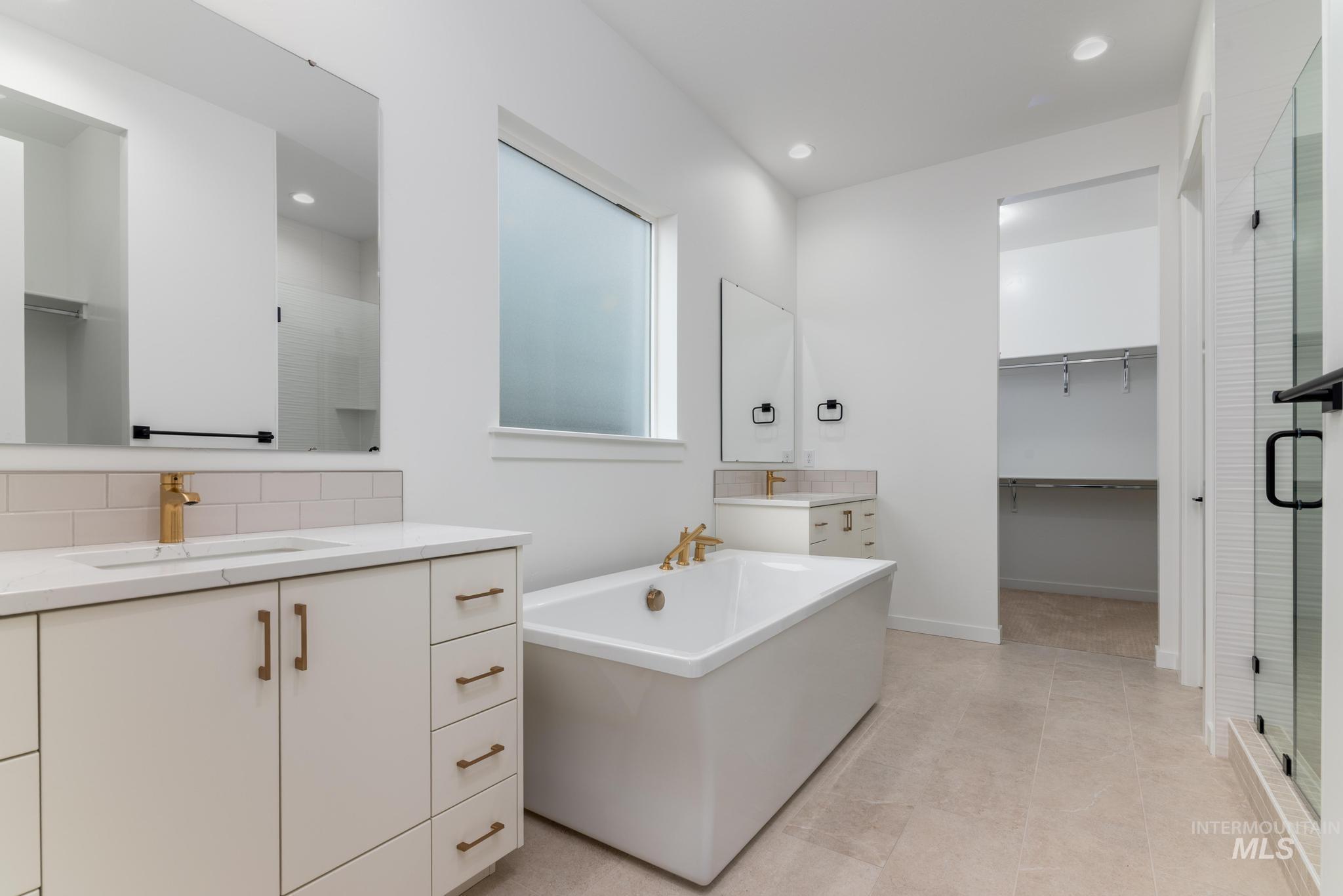 Full bathroom featuring a spacious closet, a stall shower, two vanities, a freestanding bath, and recessed lighting