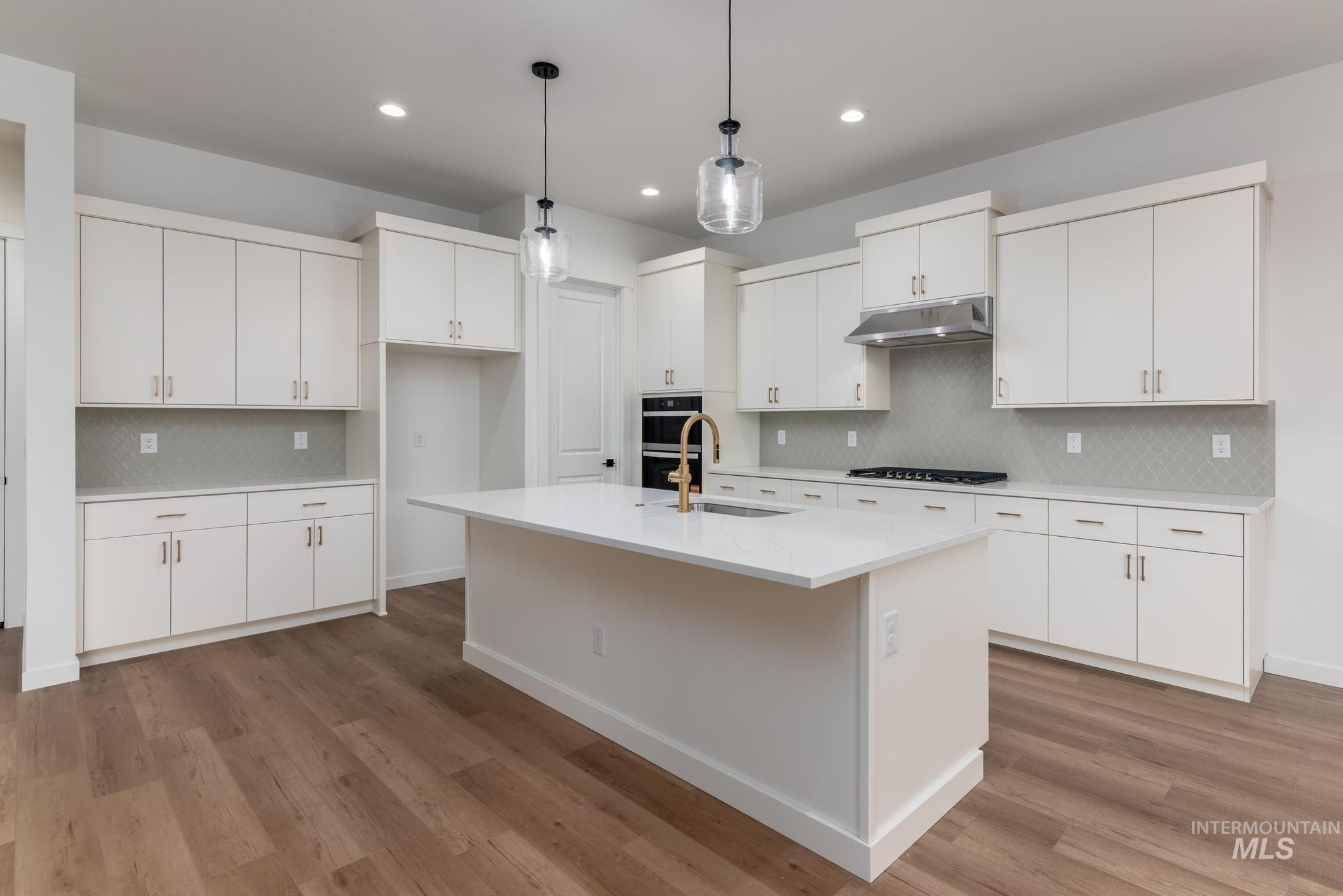 Kitchen with decorative backsplash, decorative light fixtures, white cabinetry, a center island with sink, and recessed lighting