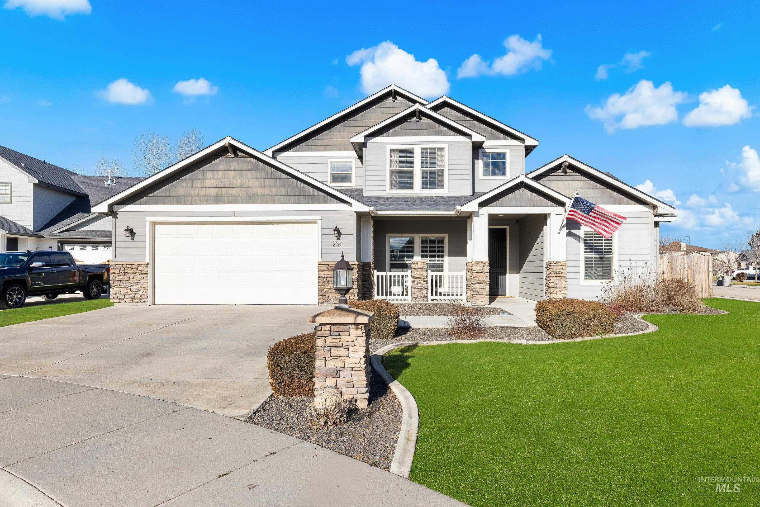 Craftsman-style house featuring stone siding, a front lawn, covered porch, concrete driveway, and a garage