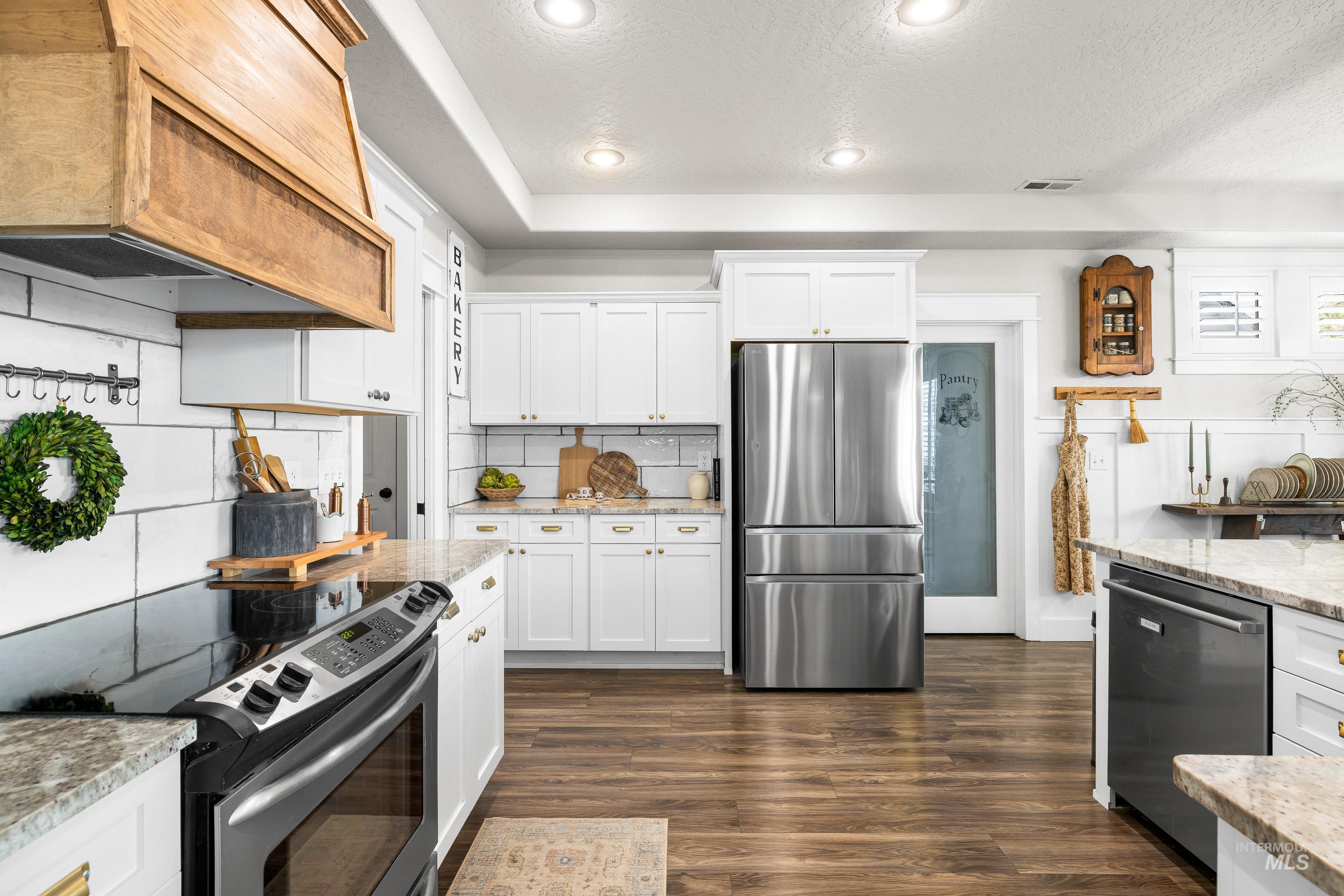 Kitchen featuring appliances with stainless steel finishes, white cabinets, backsplash, dark wood-style floors, and a textured ceiling