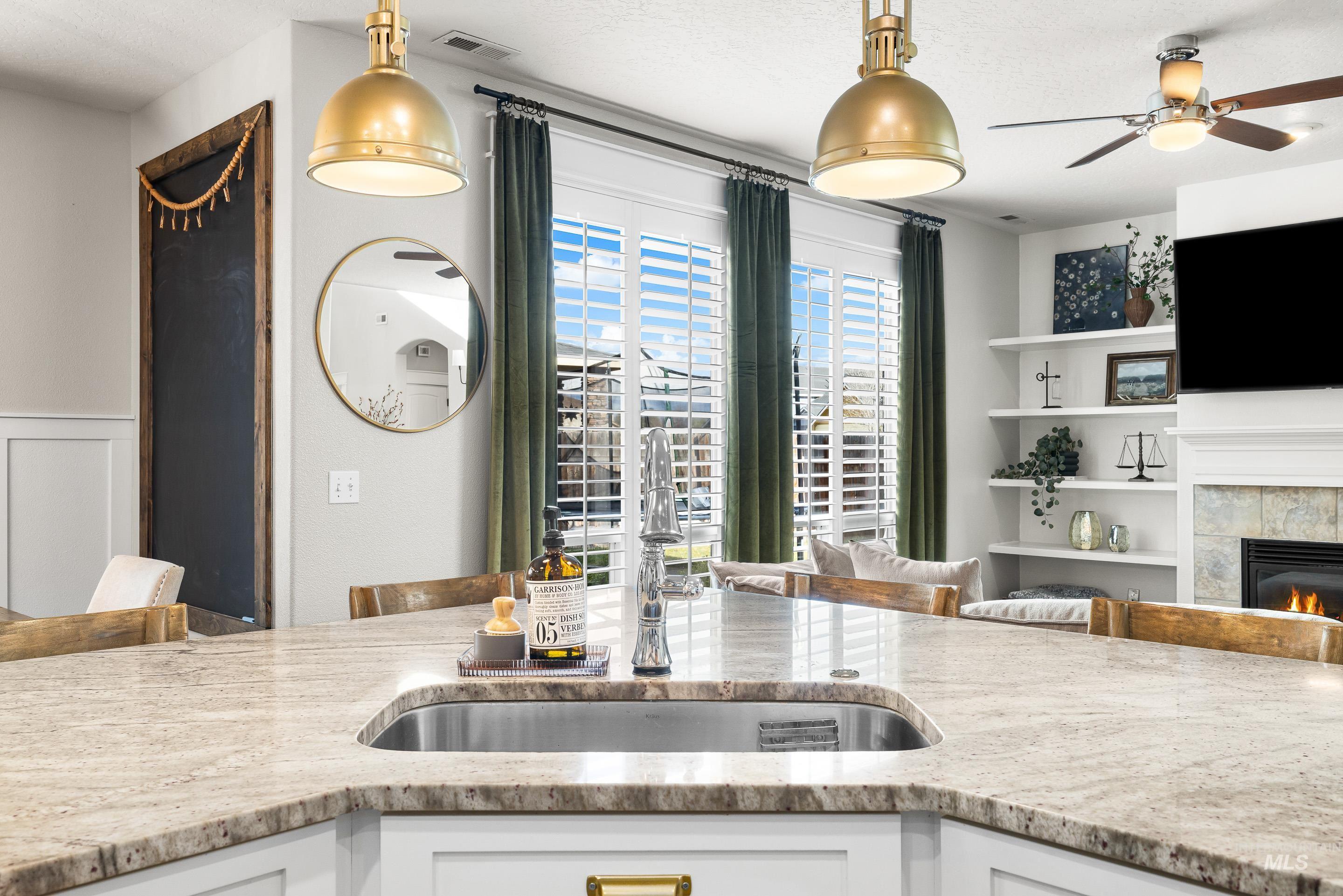Kitchen with open floor plan, light stone counters, a ceiling fan, a tile fireplace, and white cabinets