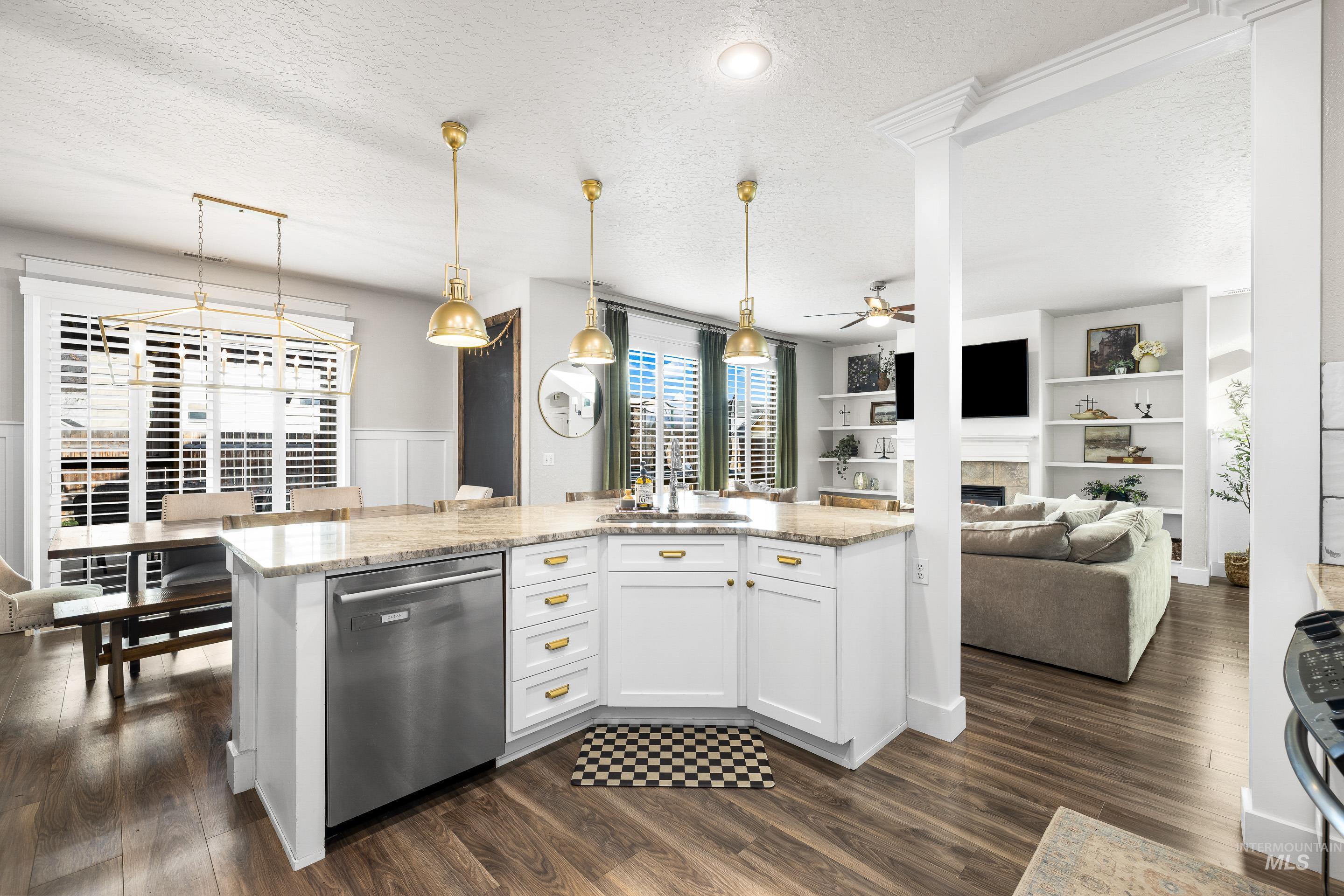 Kitchen featuring a textured ceiling, a tiled fireplace, decorative light fixtures, white cabinets, and light stone counters