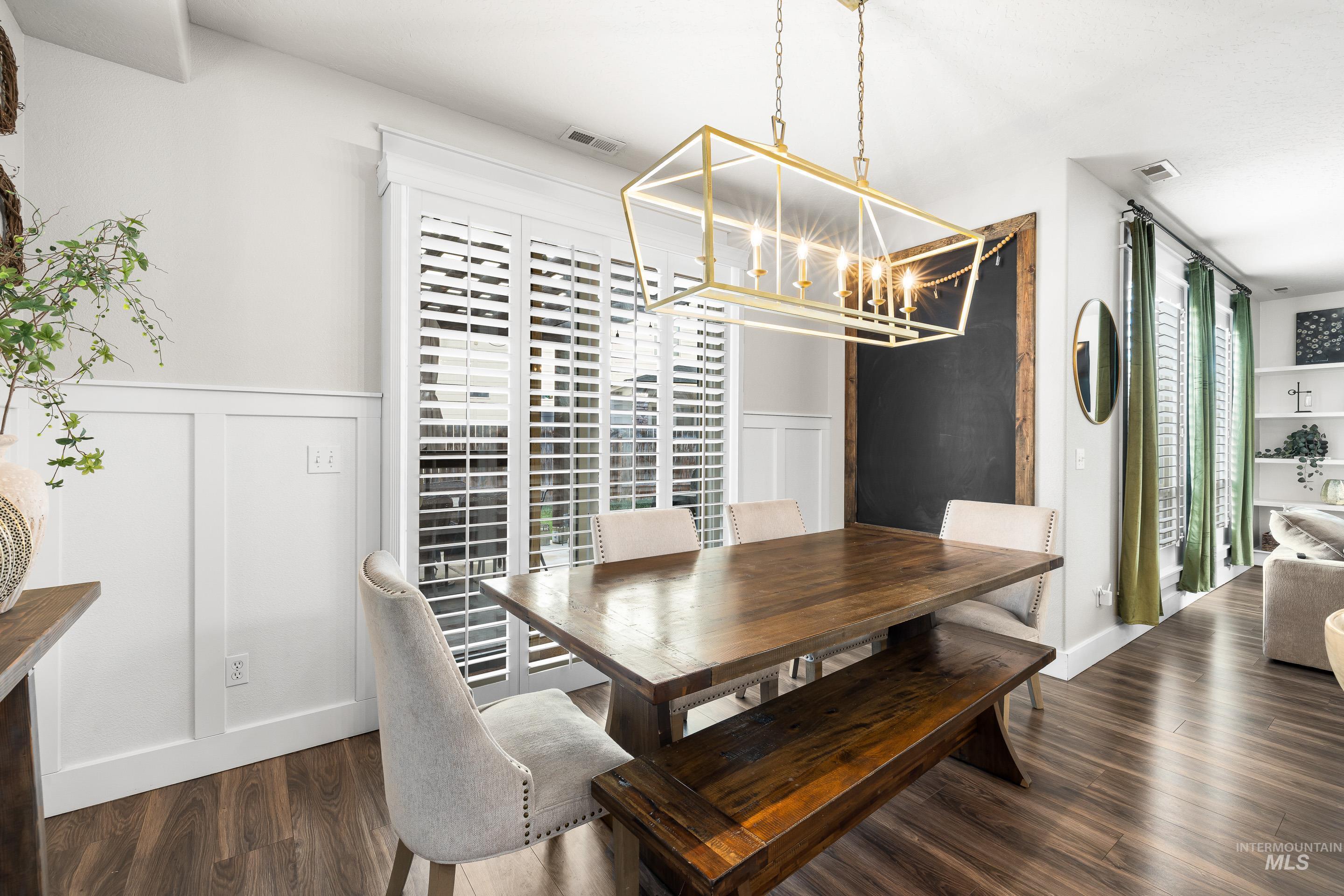 Dining space featuring dark wood finished floors, a decorative wall, a chandelier, and a wainscoted wall