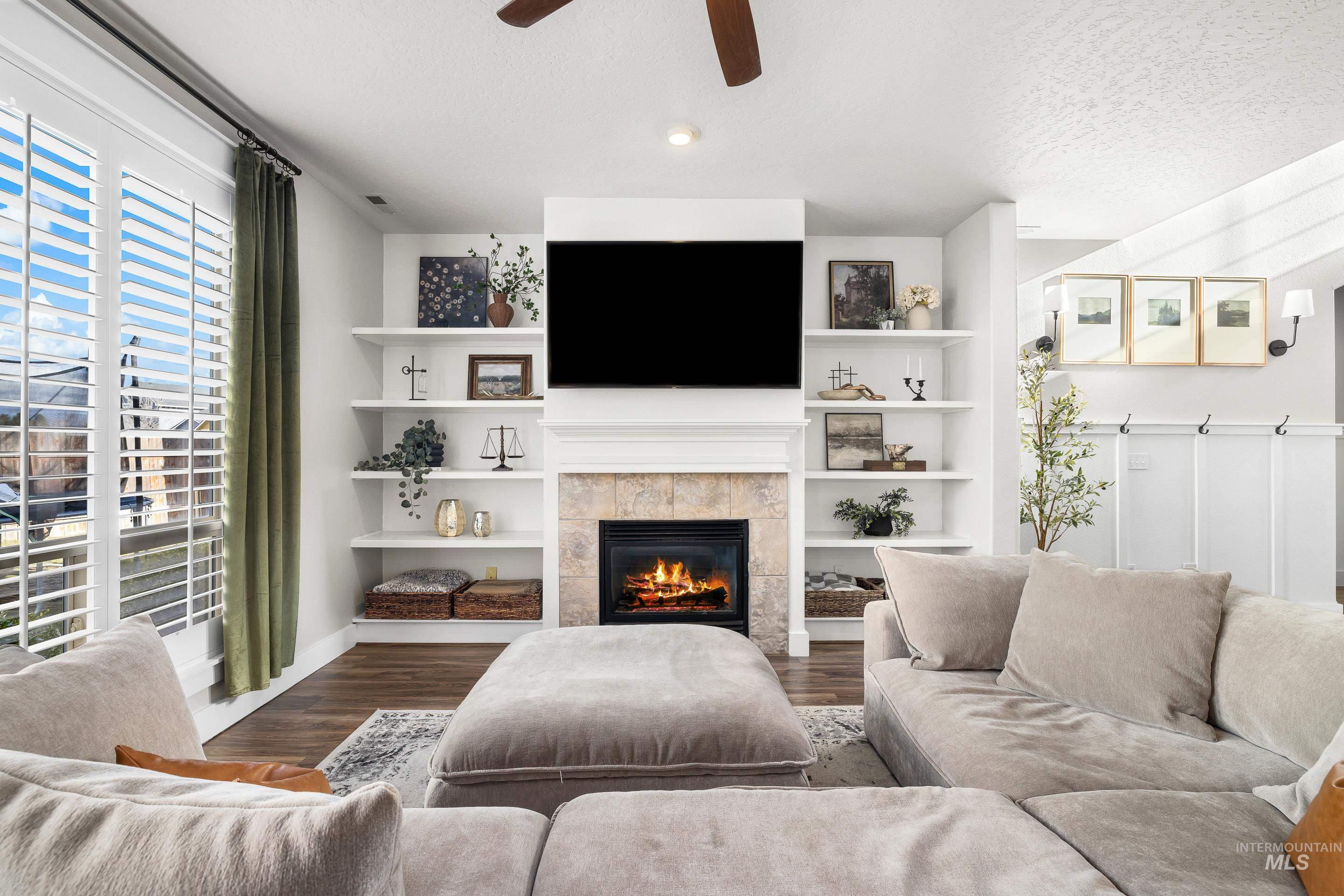 Living area featuring wood finished floors, a tile fireplace, ceiling fan, and a textured ceiling
