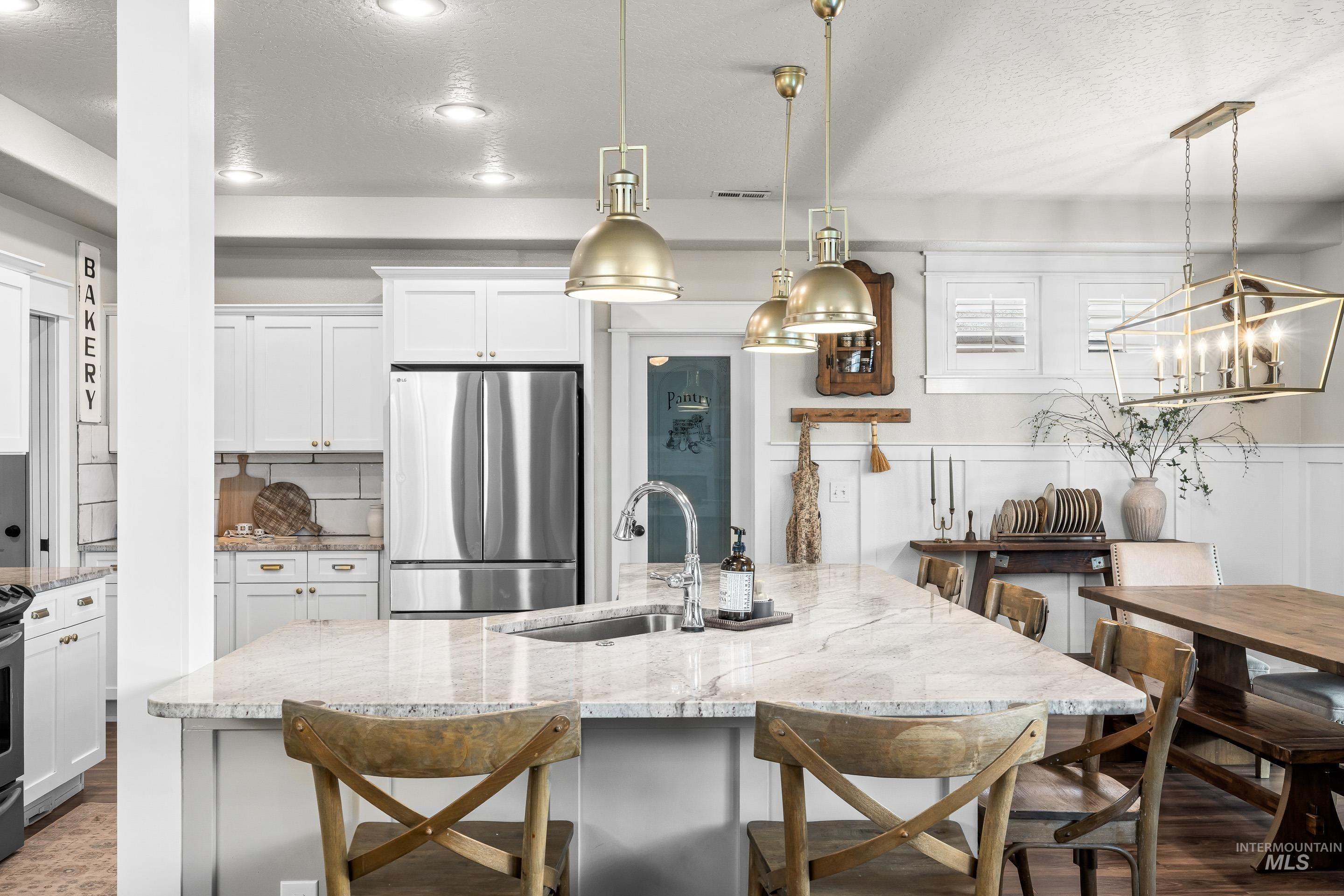 Kitchen featuring a kitchen breakfast bar, a textured ceiling, freestanding refrigerator, decorative light fixtures, and light stone counters