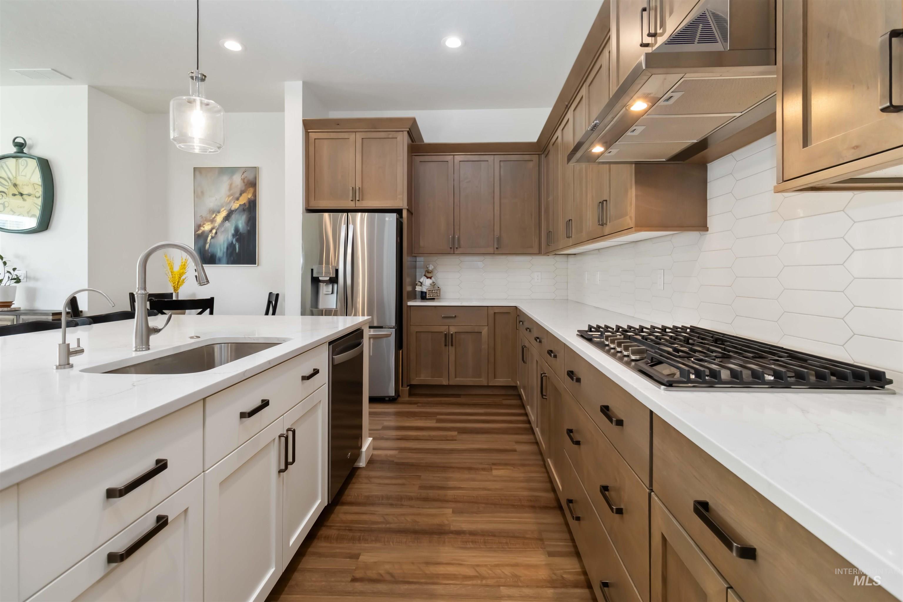 Kitchen with gas cook top built in oven, under cabinet range hood, wood-type flooring, light quartz countertops, hanging light fixtures, and recessed lighting