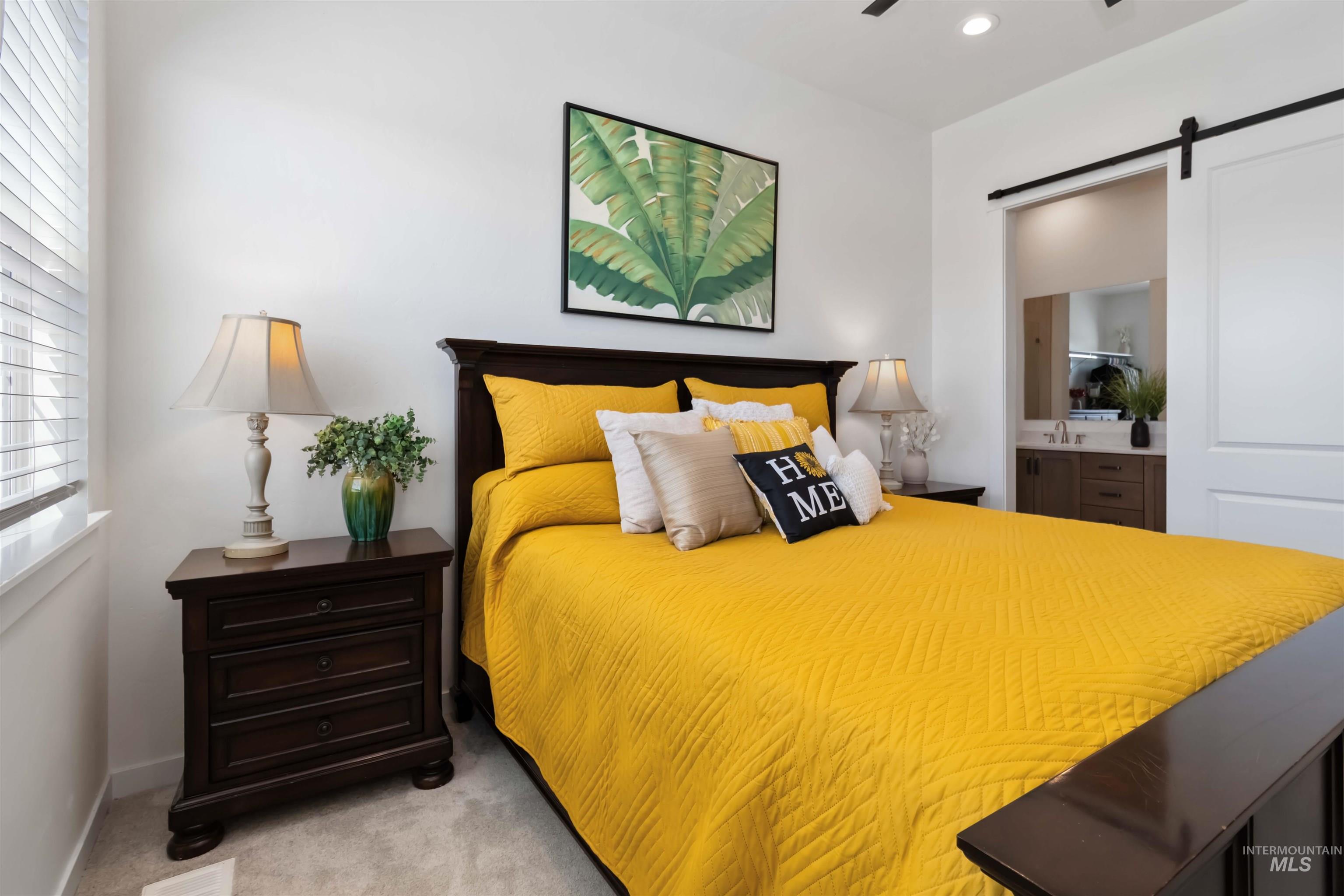 Primary Bedroom with a barn door, light colored carpet, and connected bathroom