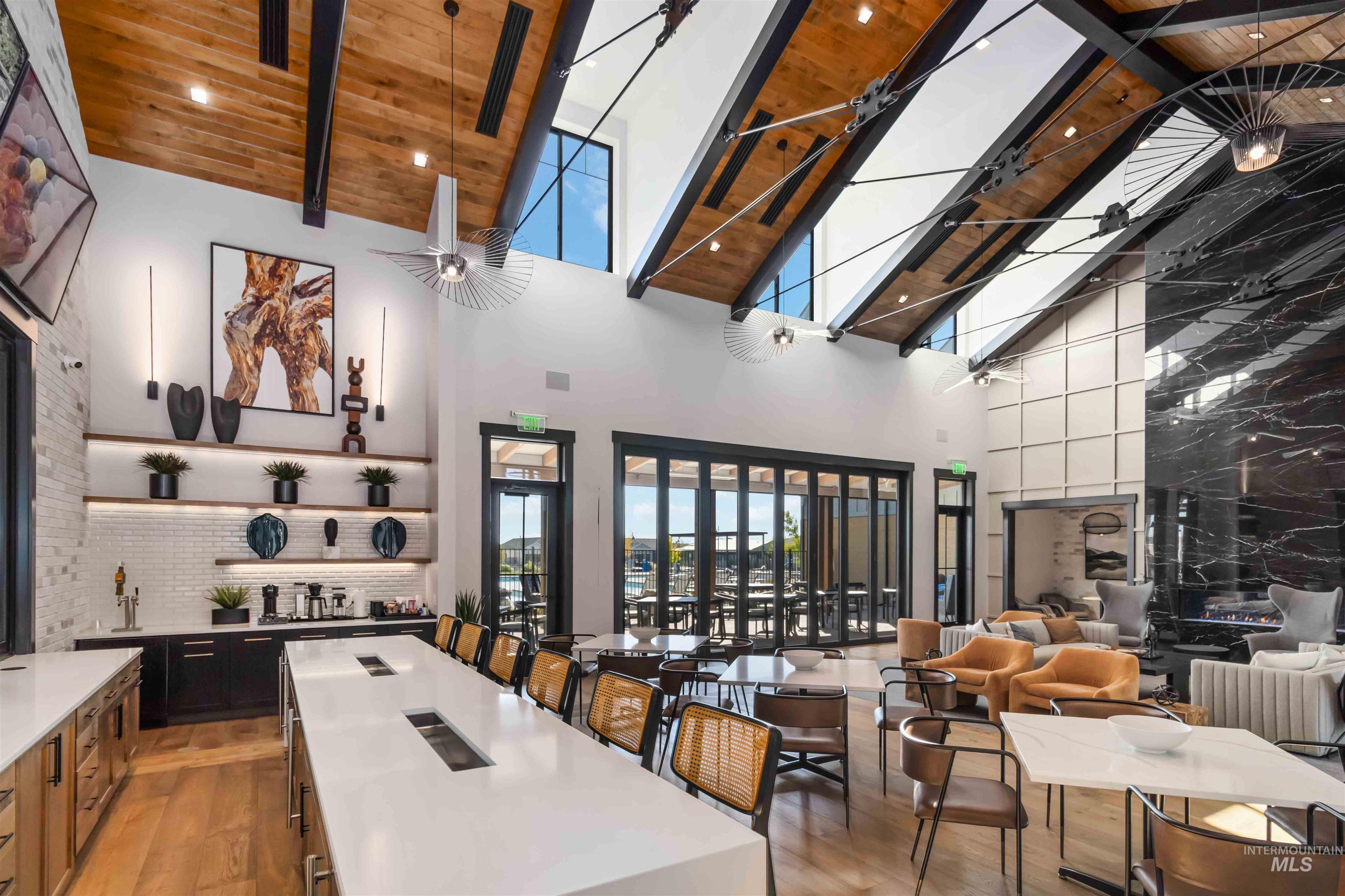 Club House kitchen & serving area with high vaulted ceiling, light stone countertops, a large island with sink, open shelves, and a bar area. Catering Kitchen is off to the side (not in photo)