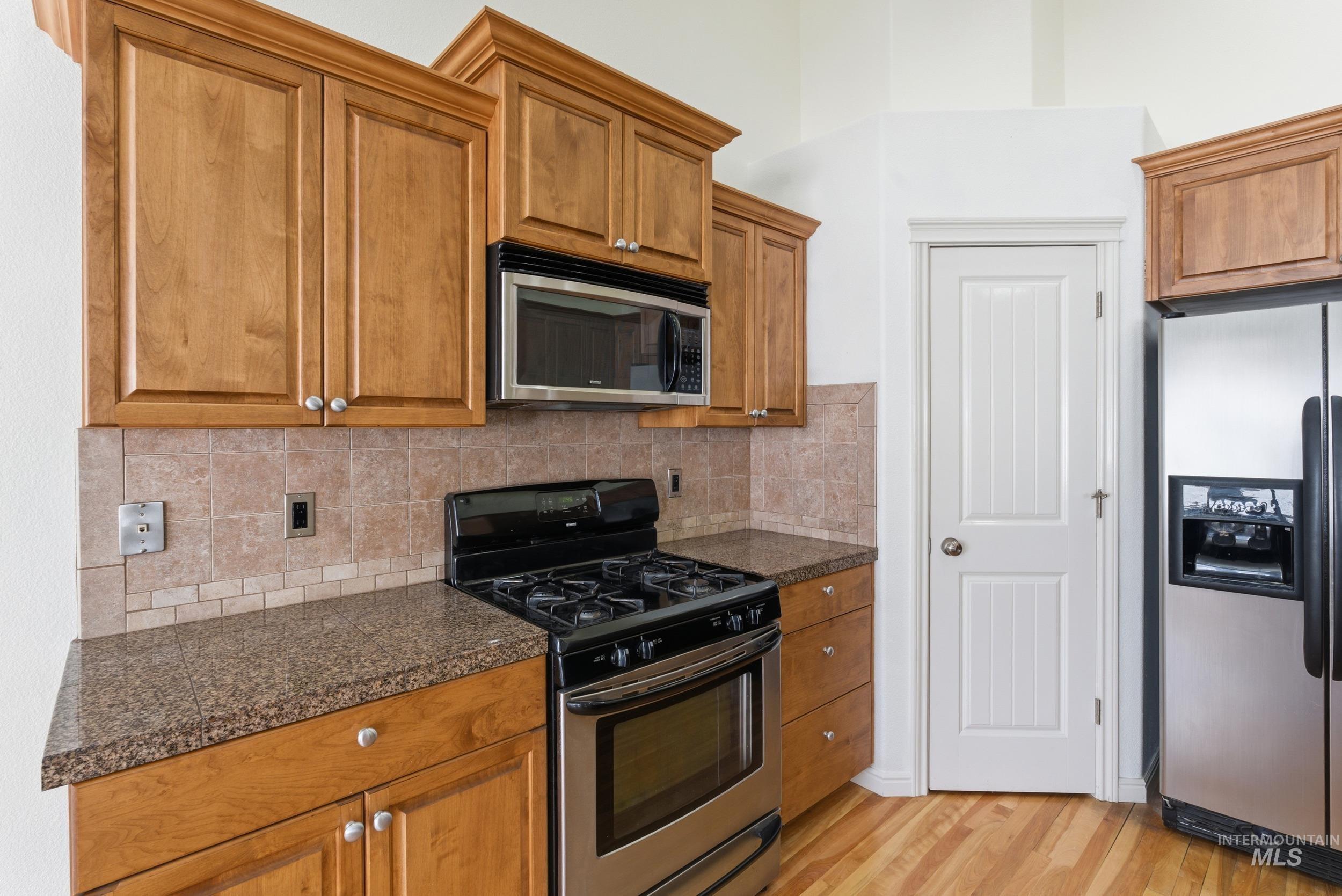 Kitchen with appliances with stainless steel finishes, brown cabinetry, light wood-style floors, and tile countertops