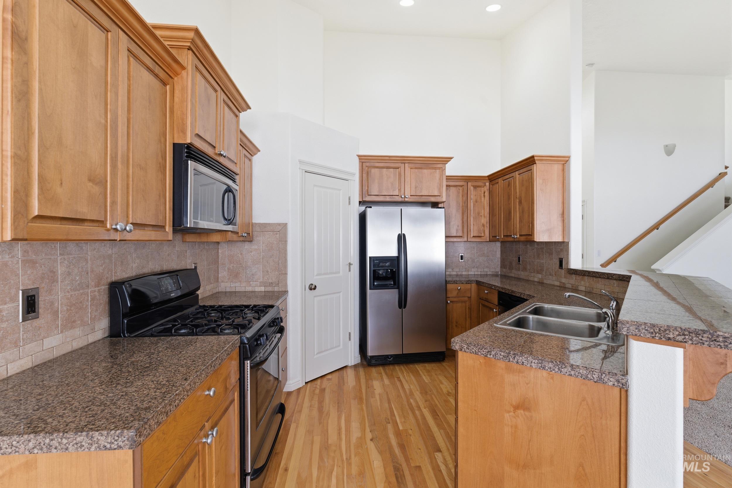 Kitchen with appliances with stainless steel finishes, a peninsula, light wood finished floors, a high ceiling, and brown cabinets