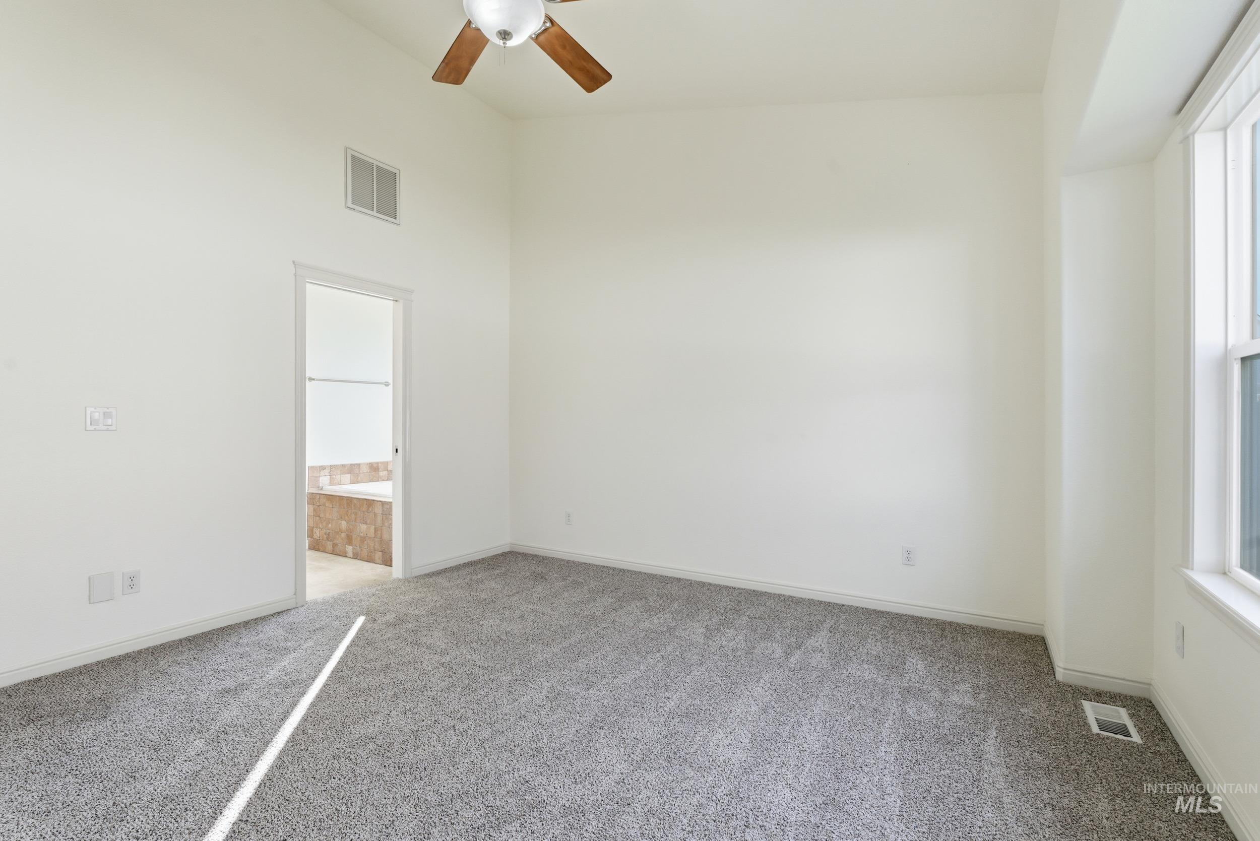 Empty room featuring light carpet, a ceiling fan, and a towering ceiling