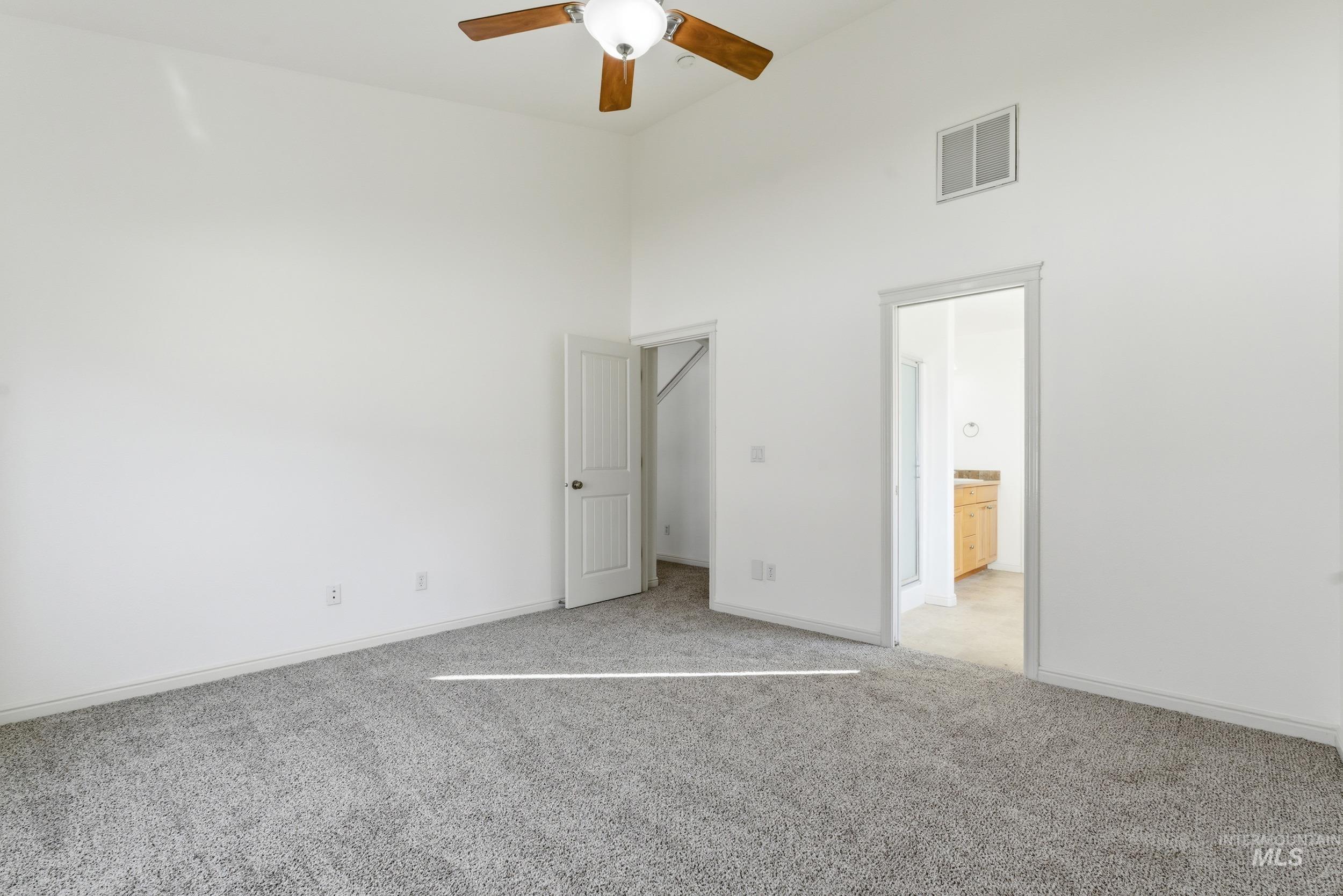 Unfurnished bedroom with a high ceiling, light carpet, ensuite bathroom, and ceiling fan