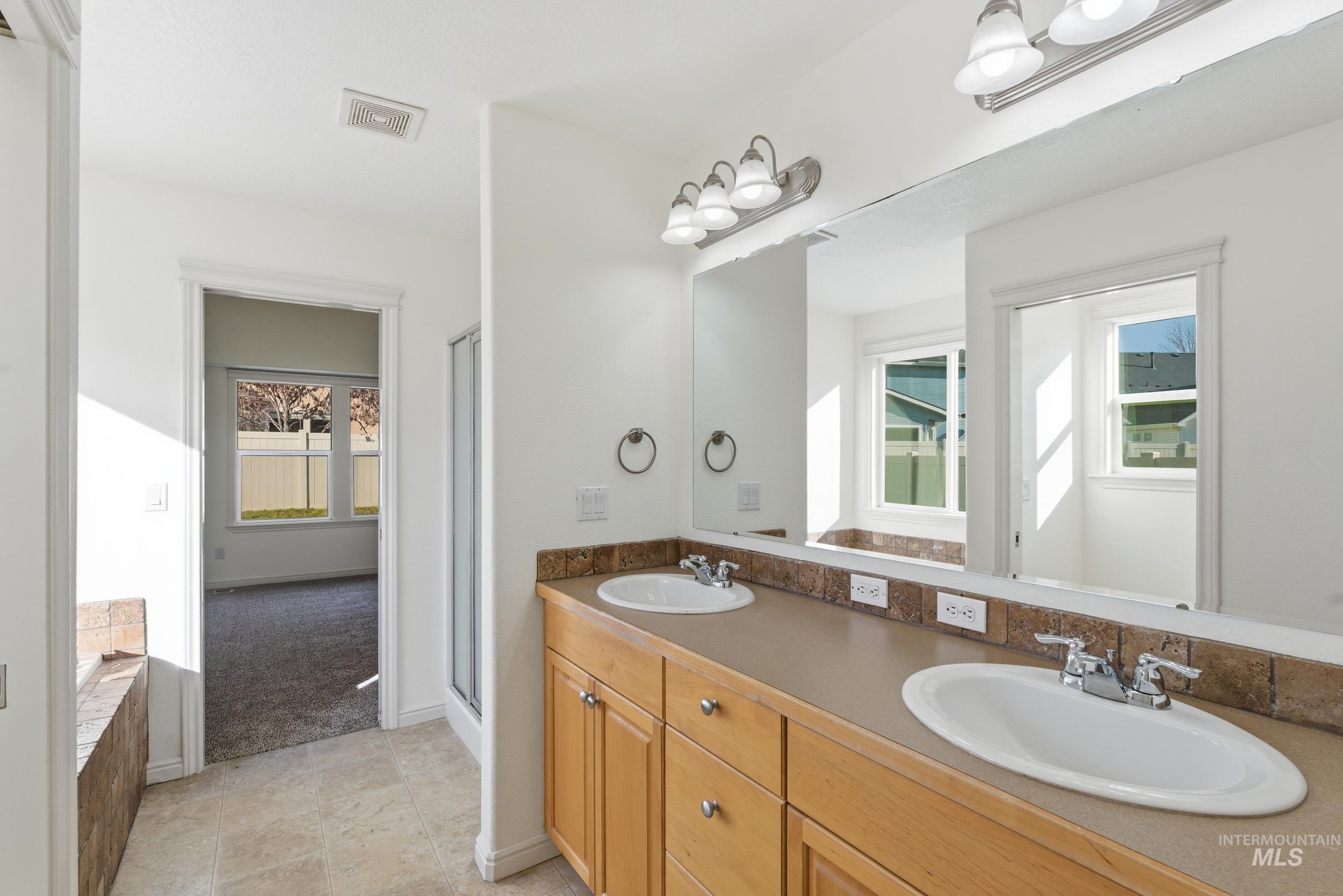 Bathroom featuring double vanity, a stall shower, light tile patterned floors, and light carpet