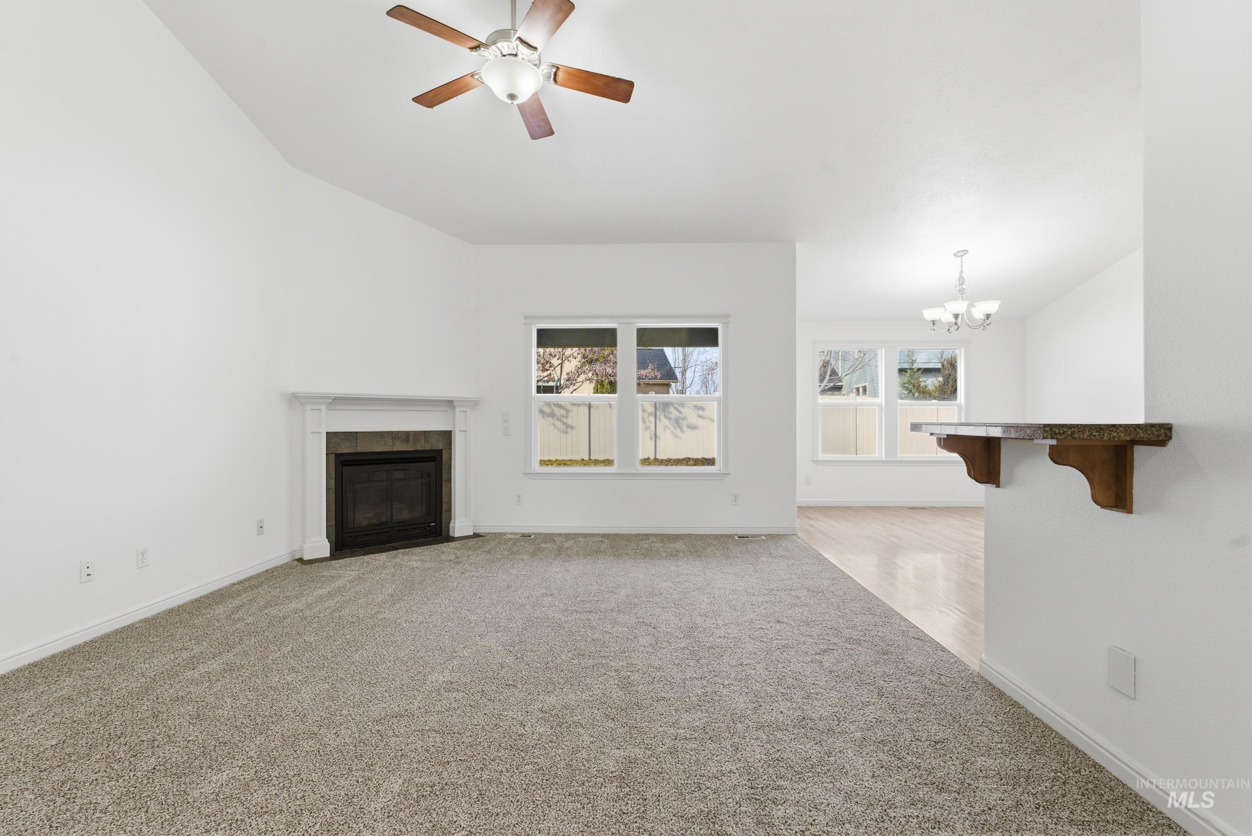 Unfurnished living room featuring light carpet, ceiling fan, a tiled fireplace, and a chandelier