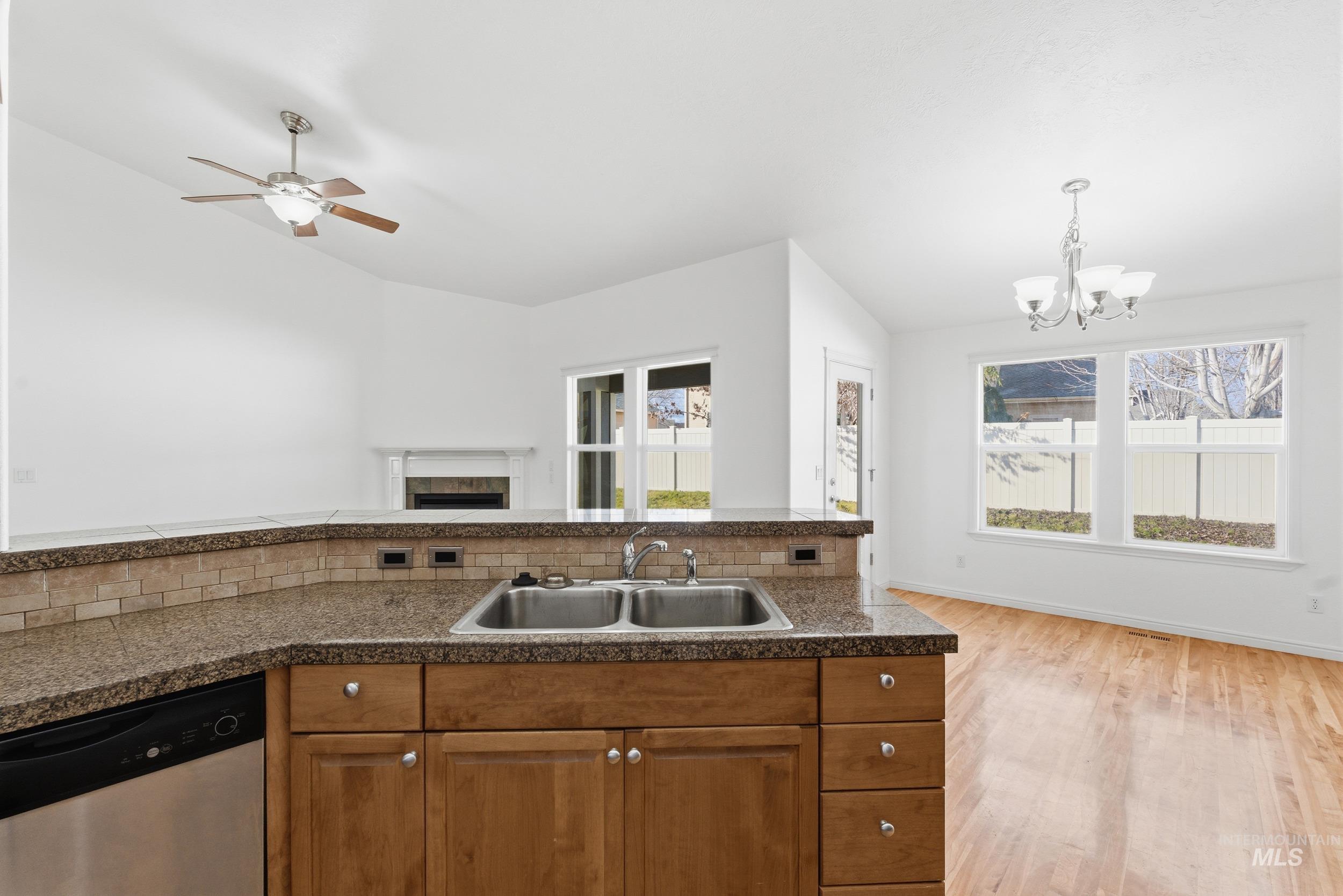 Kitchen featuring brown cabinets, stainless steel dishwasher, decorative light fixtures, light wood-style flooring, and a chandelier