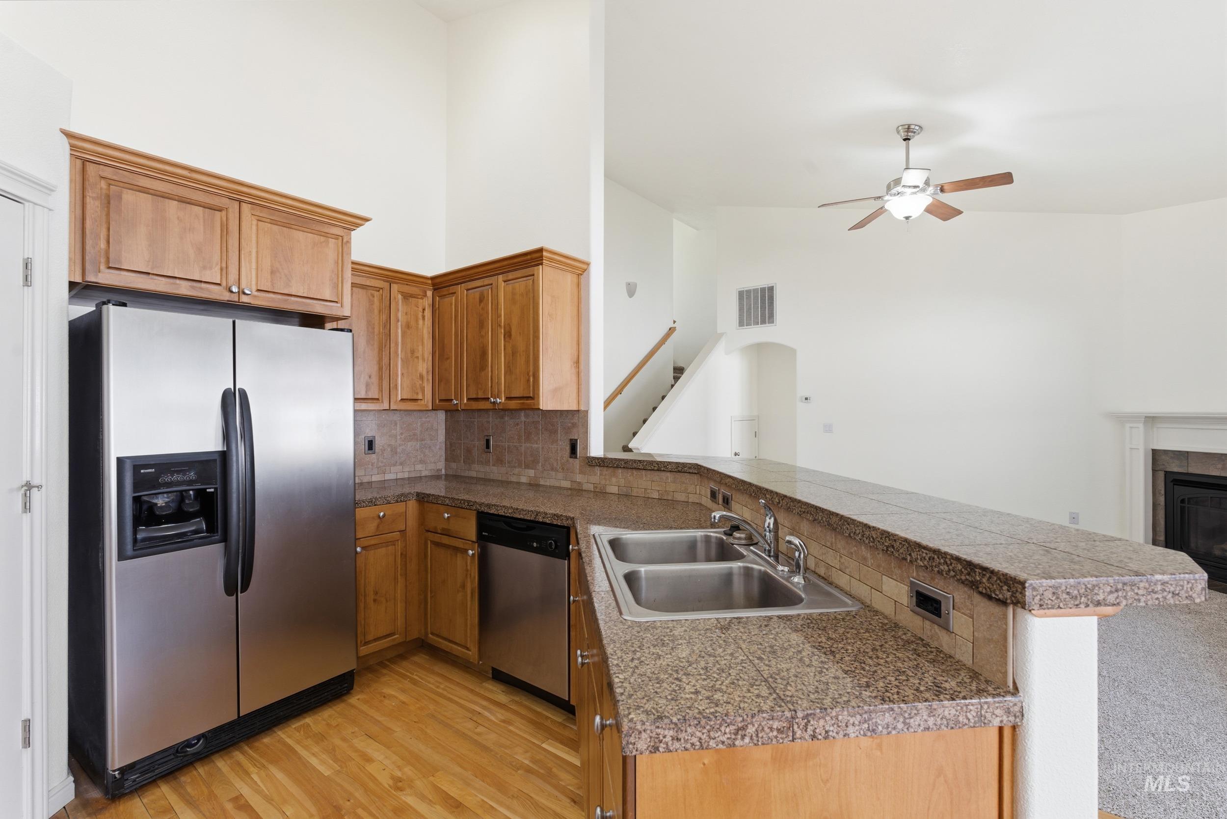Kitchen with a peninsula, appliances with stainless steel finishes, brown cabinetry, tile countertops, and open floor plan