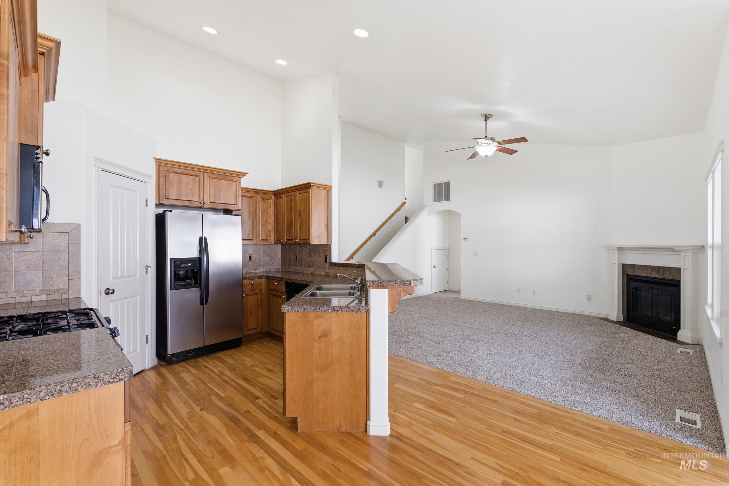 Kitchen featuring high vaulted ceiling, appliances with stainless steel finishes, tasteful backsplash, a peninsula, and brown cabinets
