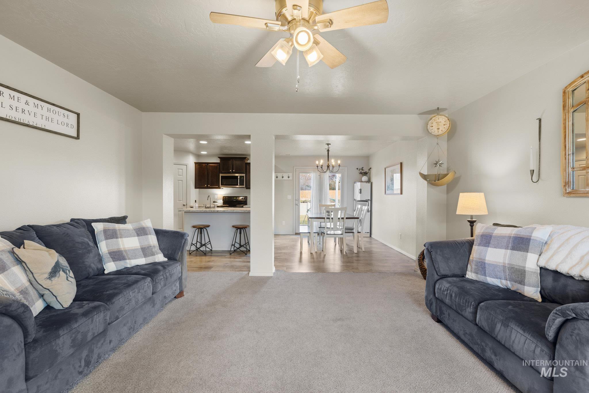 Living area with ceiling fan, light colored carpet, and a chandelier