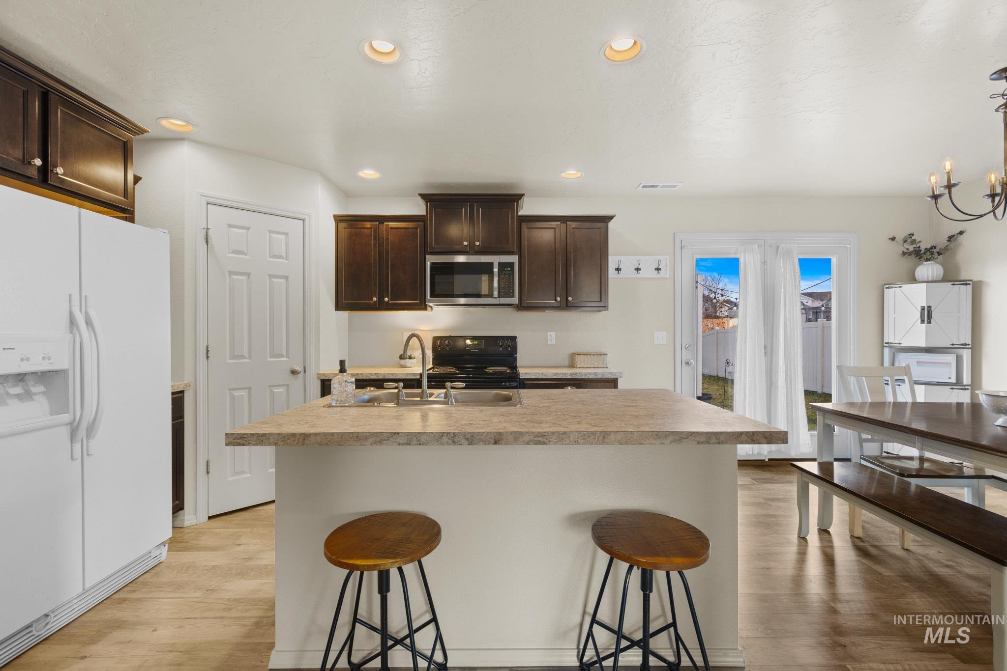 Kitchen with white fridge with ice dispenser, dark brown cabinetry, a kitchen island with sink, a kitchen bar, and light countertops
