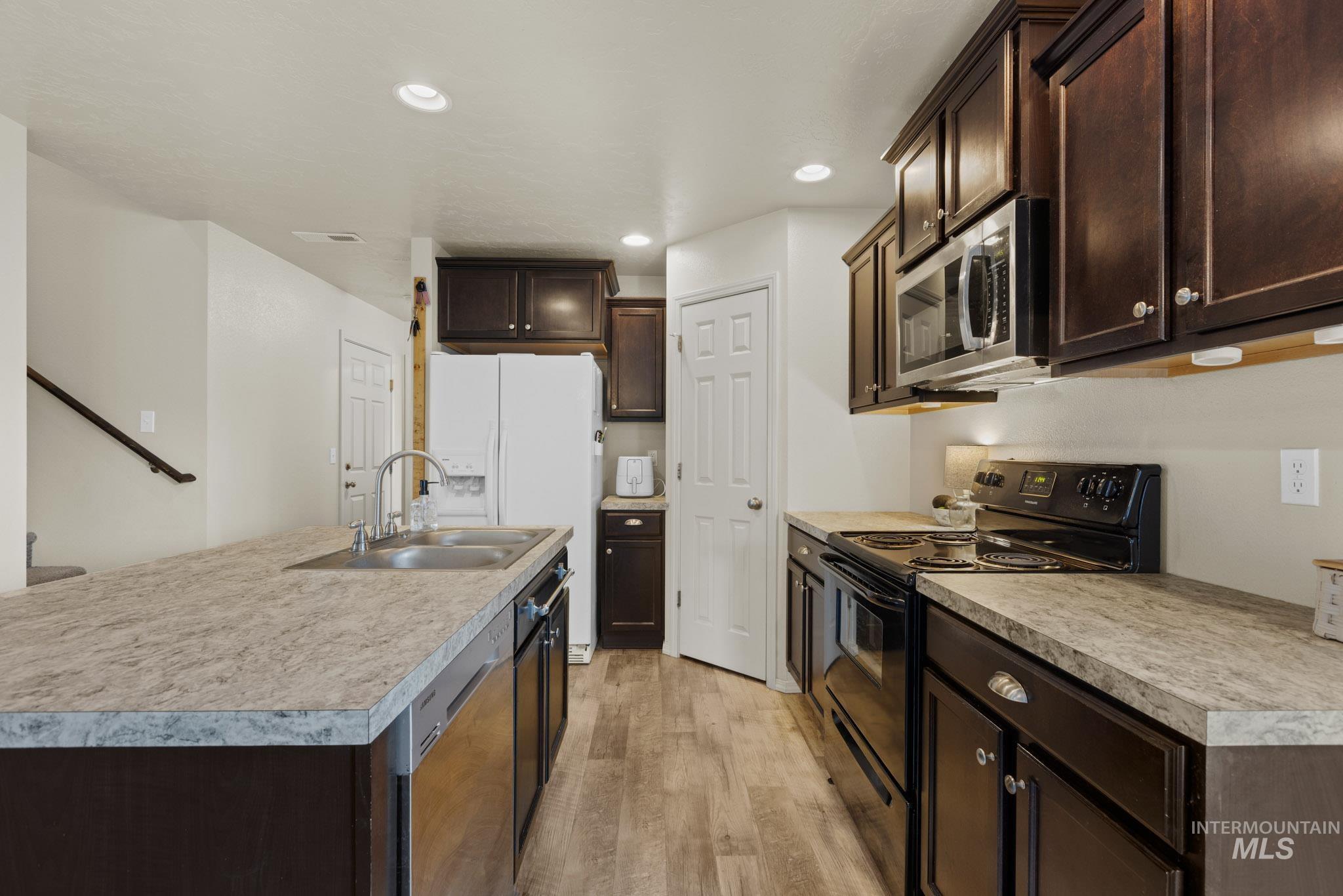 Kitchen with dark brown cabinetry, stainless steel appliances, recessed lighting, light countertops, and a kitchen island with sink