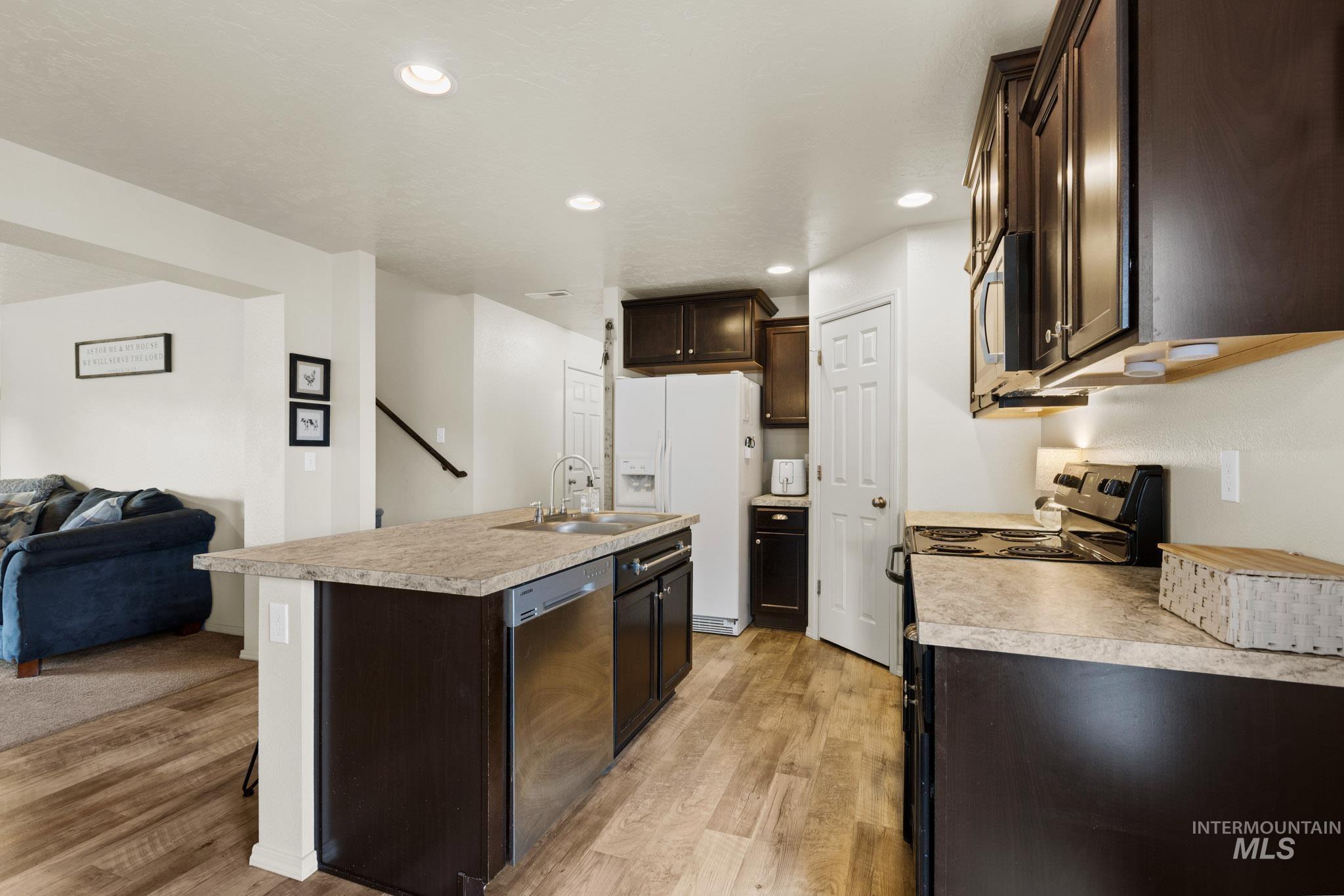 Kitchen with dark brown cabinets, open floor plan, recessed lighting, light countertops, and an island with sink