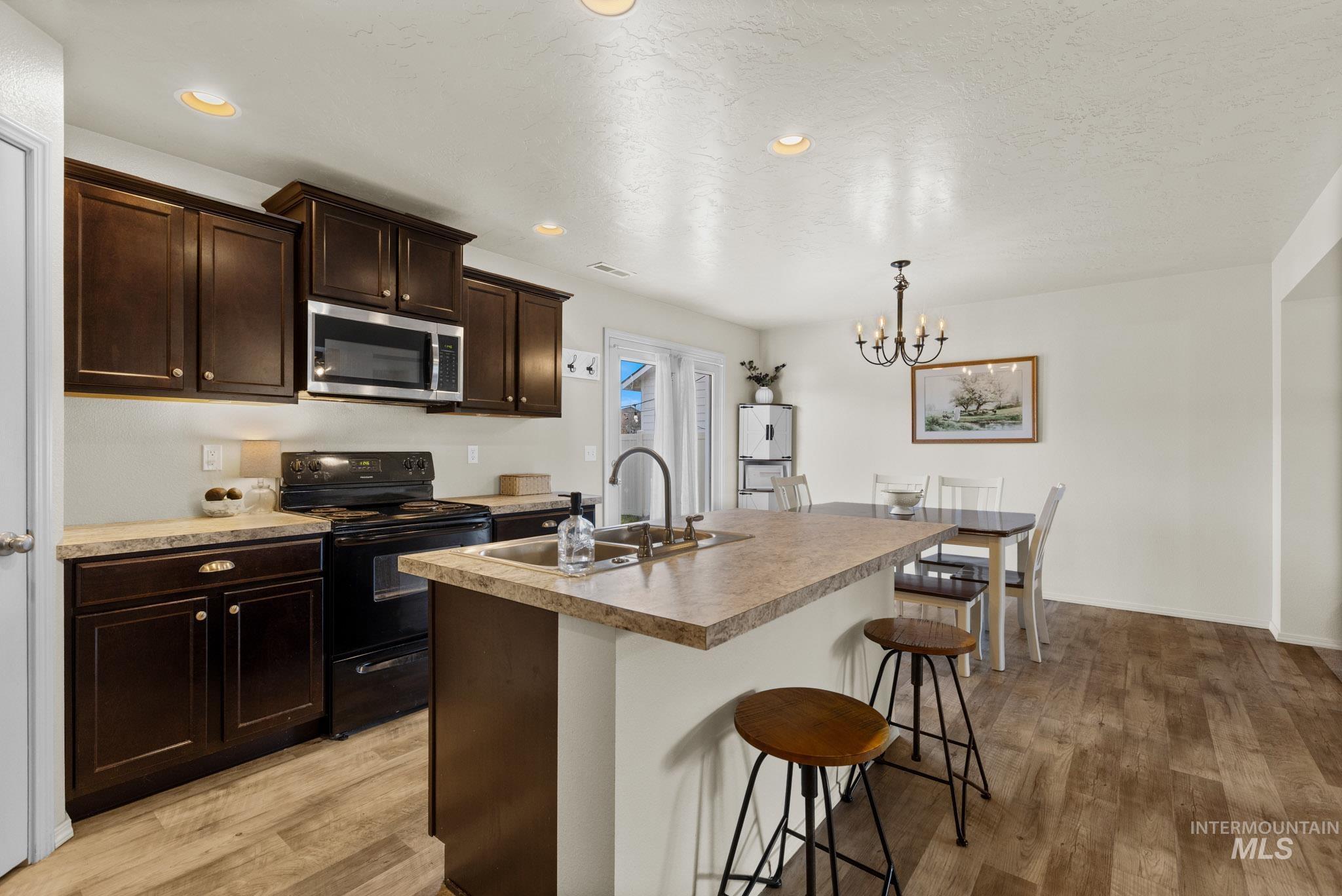 Kitchen with dark brown cabinetry, black / electric stove, an island with sink, a breakfast bar, and stainless steel microwave