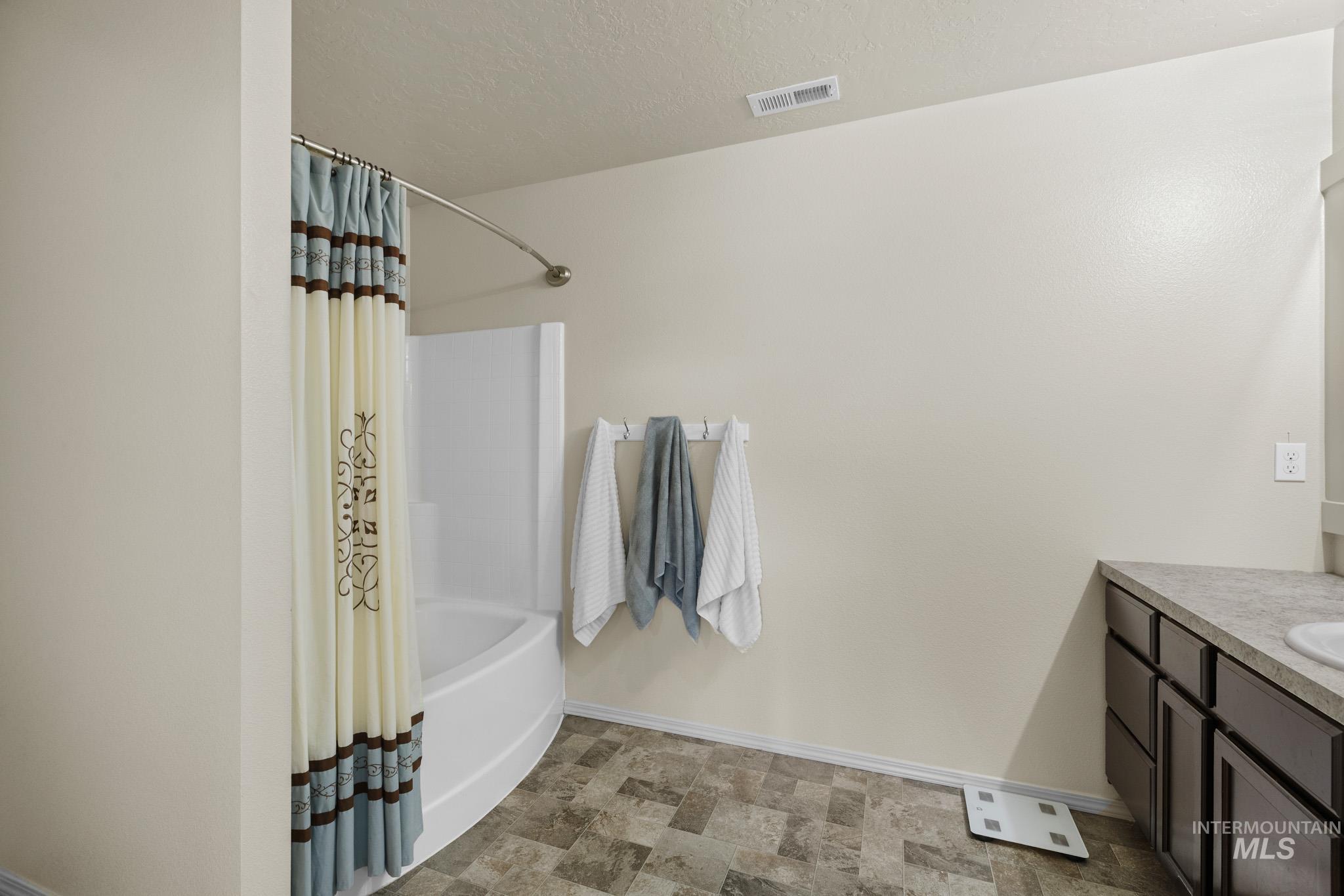 Full bath with vanity, shower / bath combo with shower curtain, stone finish floors, and a textured ceiling
