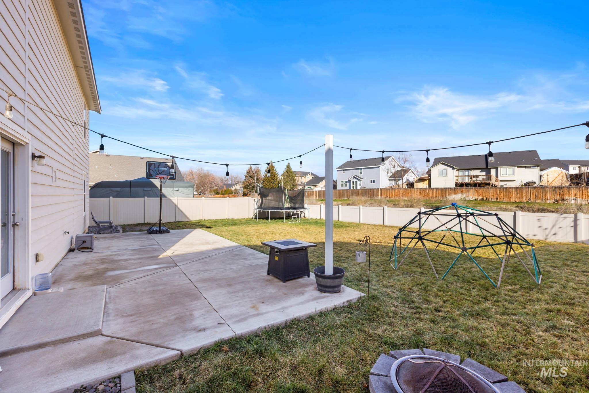 Fenced backyard with a fire pit, a trampoline, a patio area, and a residential view