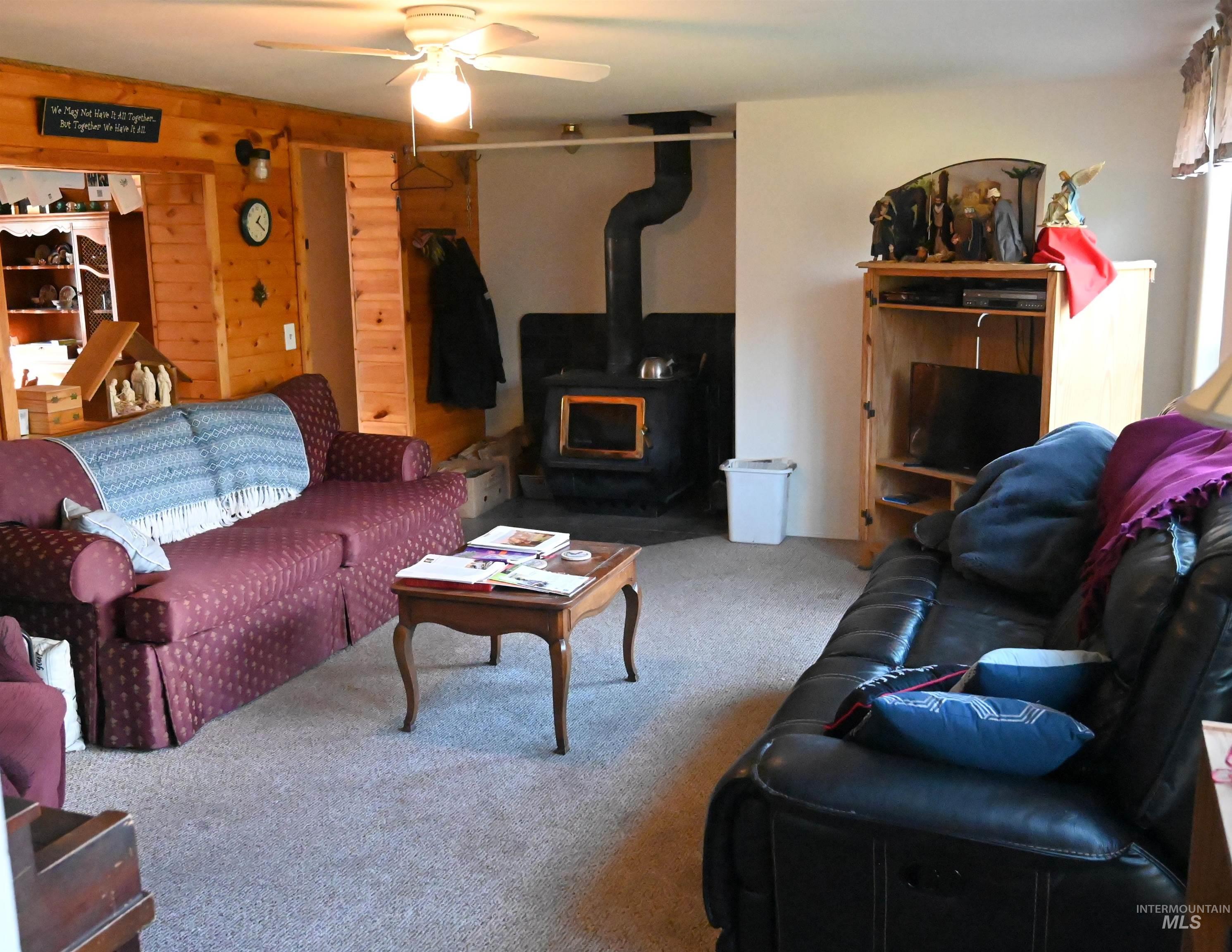 Living area featuring a wood stove, carpet floors, and a ceiling fan