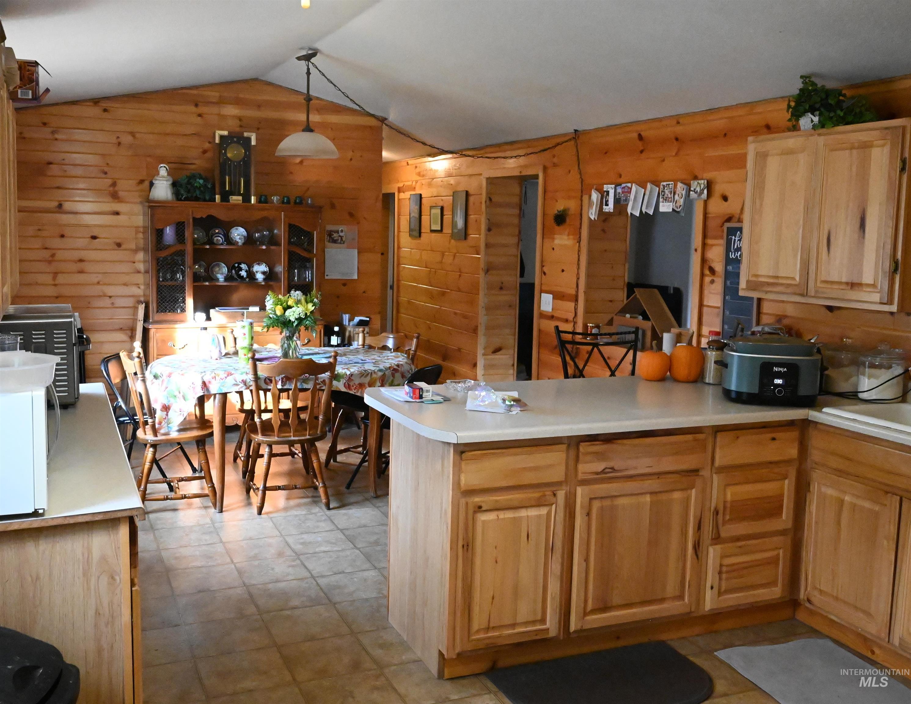 Kitchen with light countertops, lofted ceiling, a peninsula, light brown cabinetry, and wooden walls