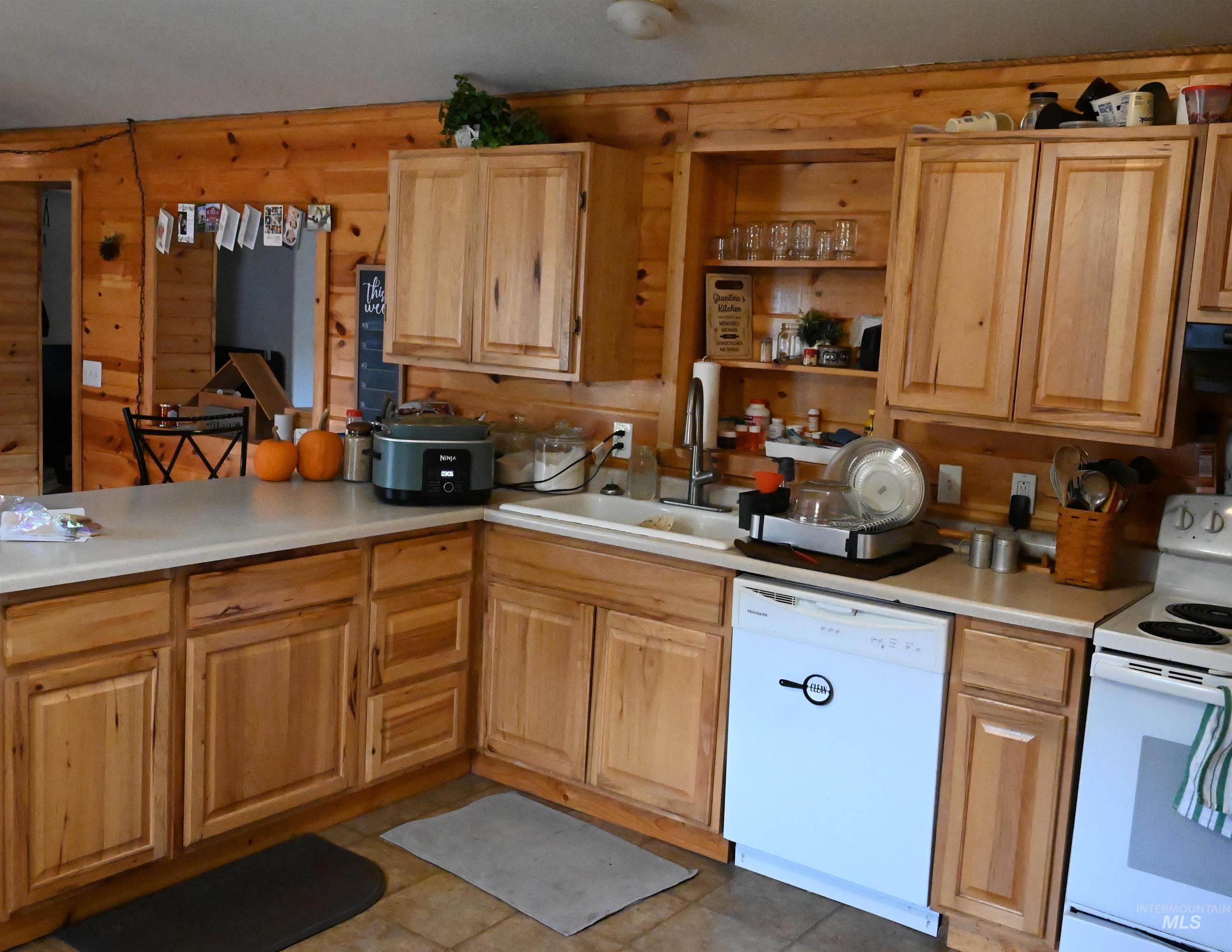 Kitchen with white appliances, light countertops, open shelves, wooden walls, and extractor fan