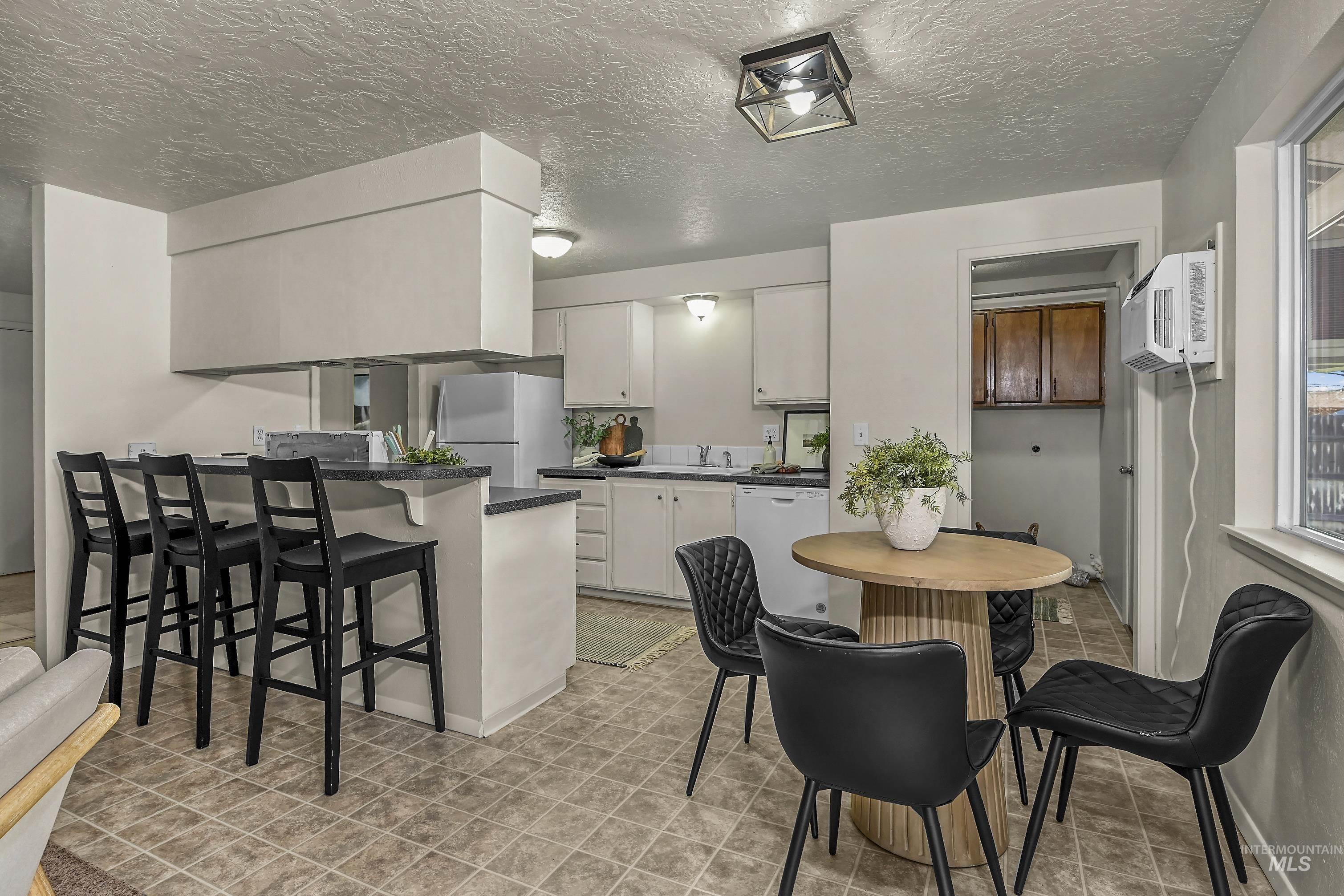 Kitchen featuring a breakfast bar area, white cabinets, dark countertops, a textured ceiling, and freestanding refrigerator
