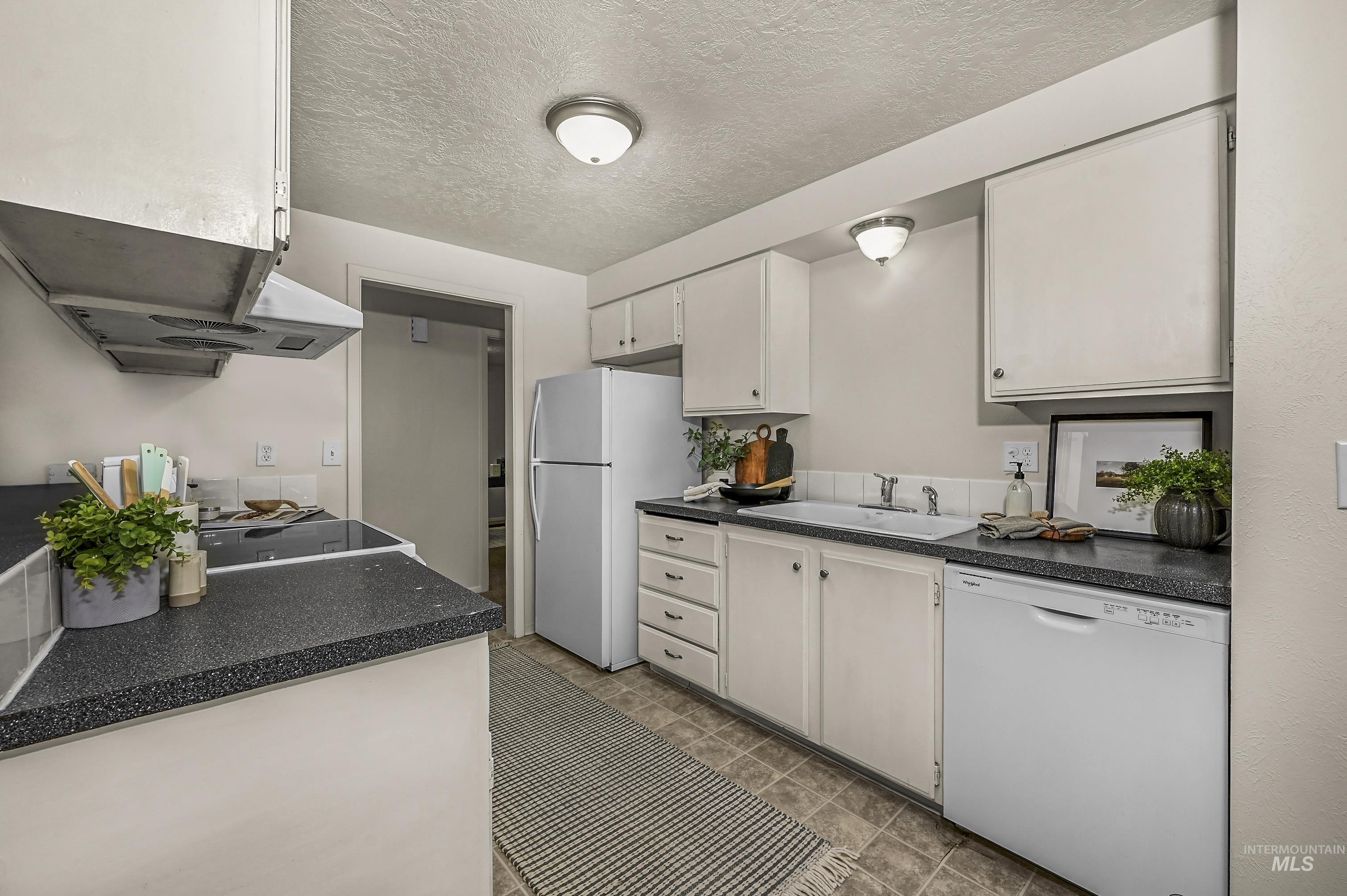 Kitchen with white appliances, a textured ceiling, dark countertops, and white cabinetry