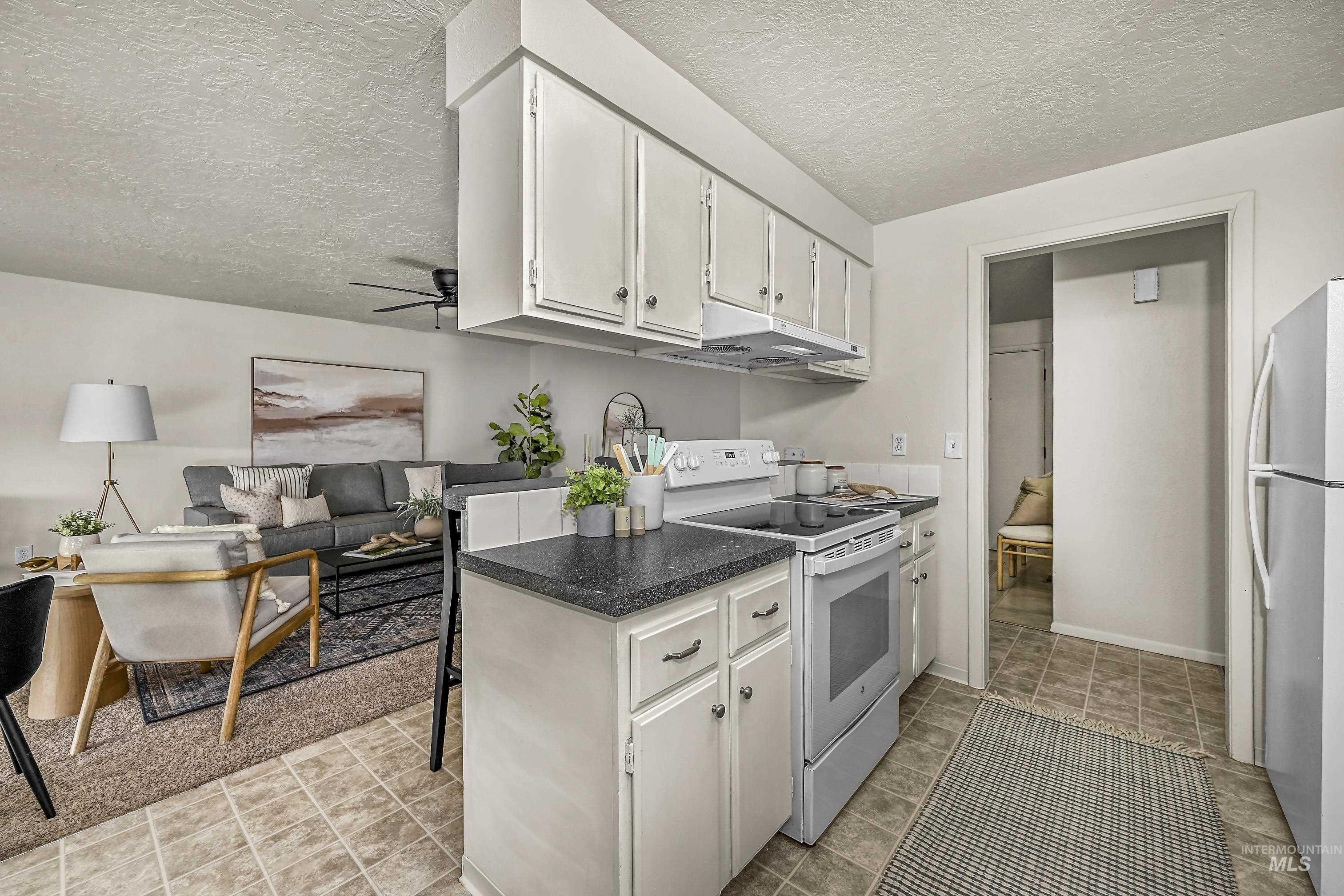 Kitchen featuring white electric range, dark countertops, a textured ceiling, freestanding refrigerator, and open floor plan