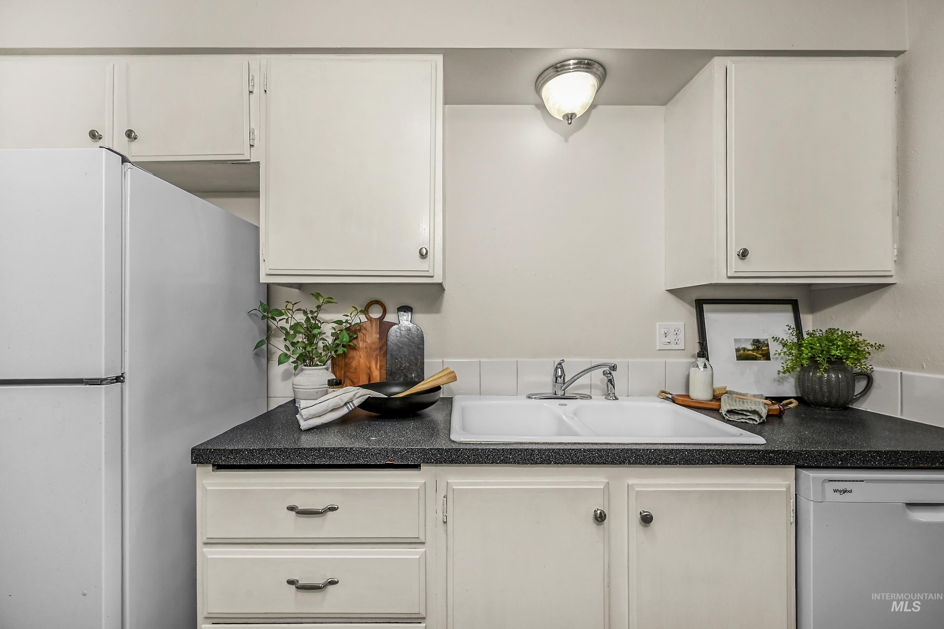 Kitchen featuring dark countertops, white appliances, and white cabinetry