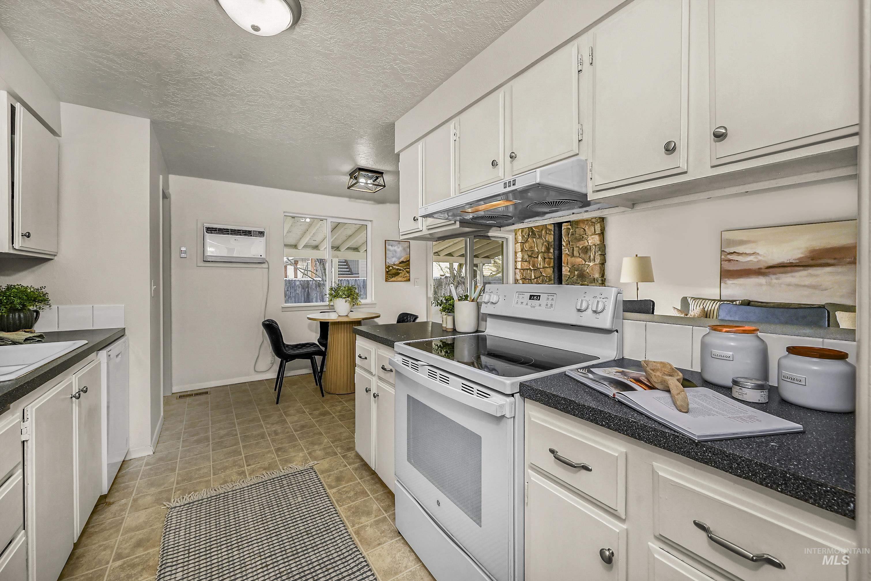 Kitchen featuring white appliances, dark countertops, a textured ceiling, white cabinets, and under cabinet range hood