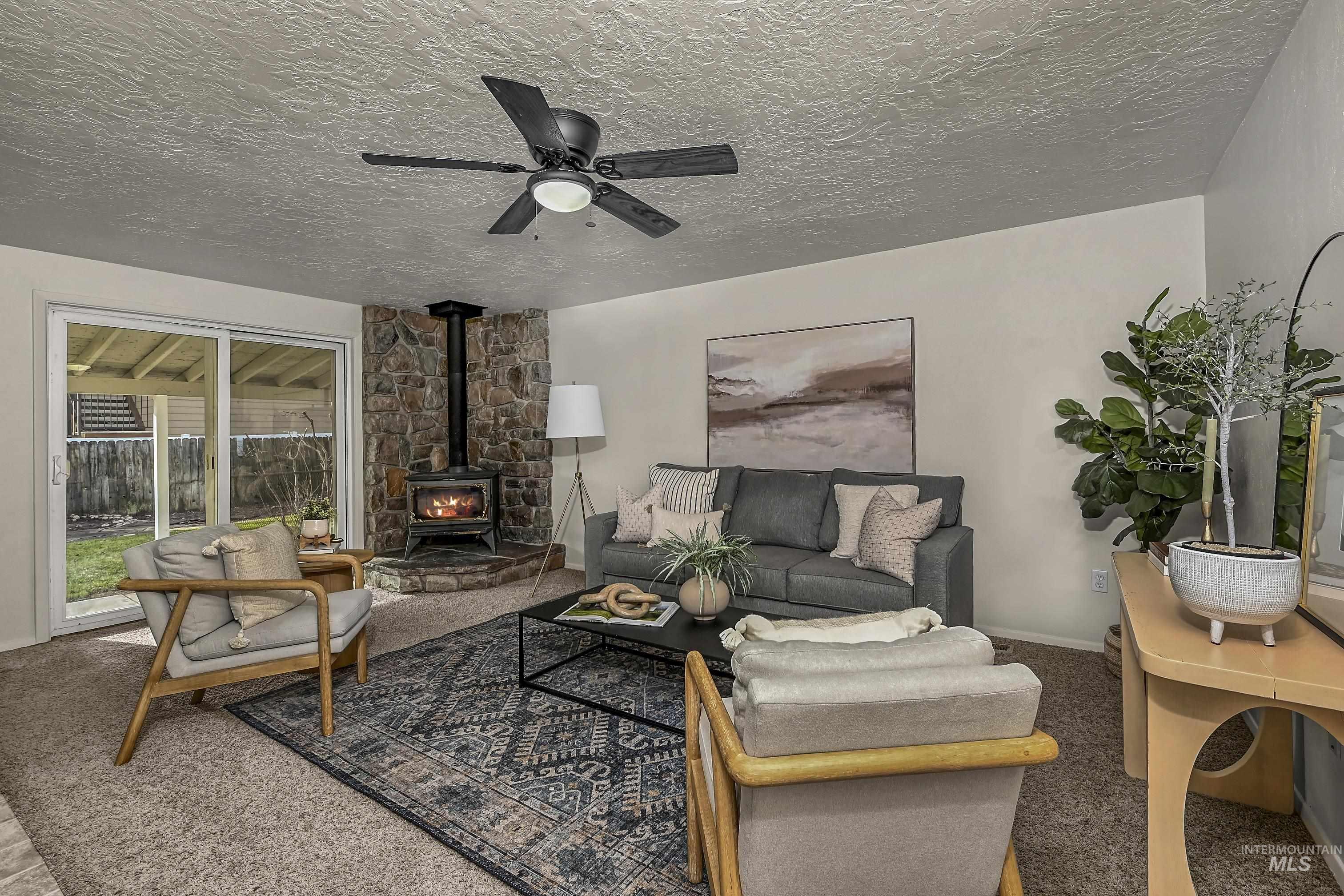 Living room featuring a wood stove, a textured ceiling, carpet, and ceiling fan