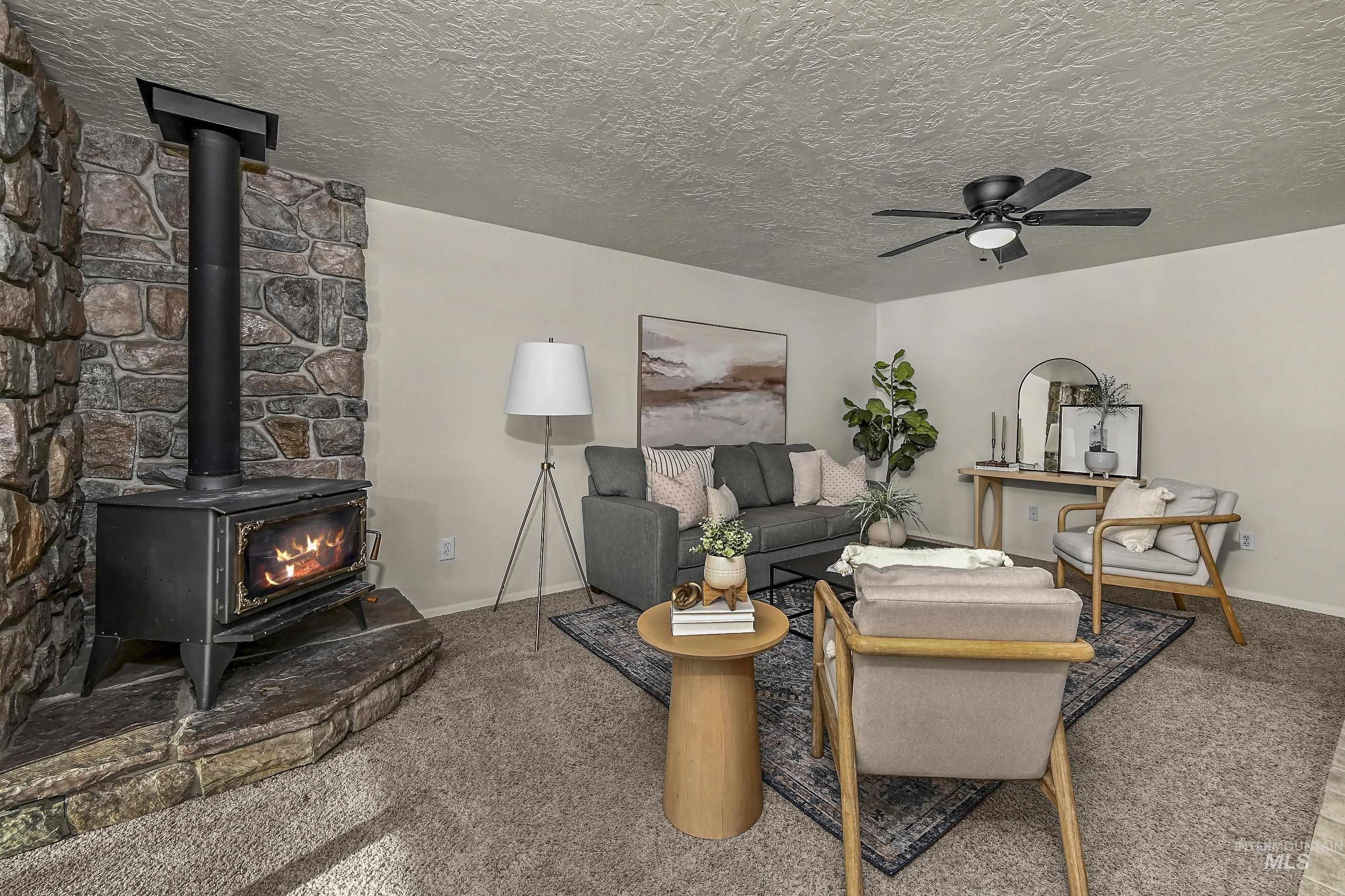 Carpeted living room with a wood stove, ceiling fan, and a textured ceiling