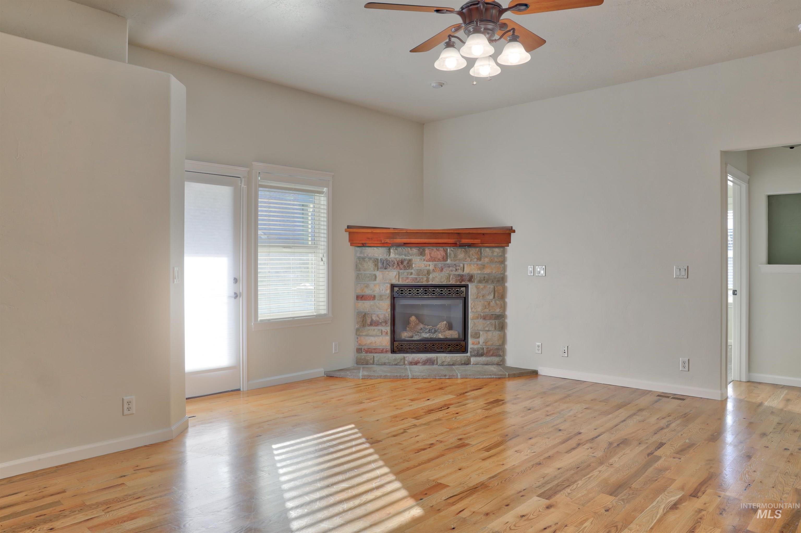 Unfurnished living room with light wood-type flooring, a stone fireplace, and ceiling fan