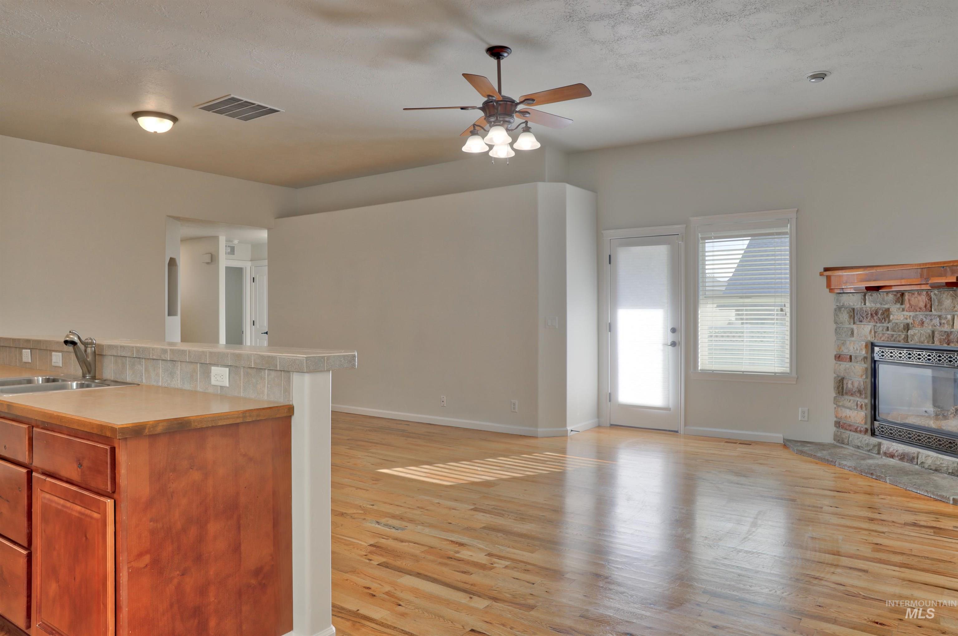 Kitchen featuring open floor plan, light countertops, a ceiling fan, light wood finished floors, and a fireplace