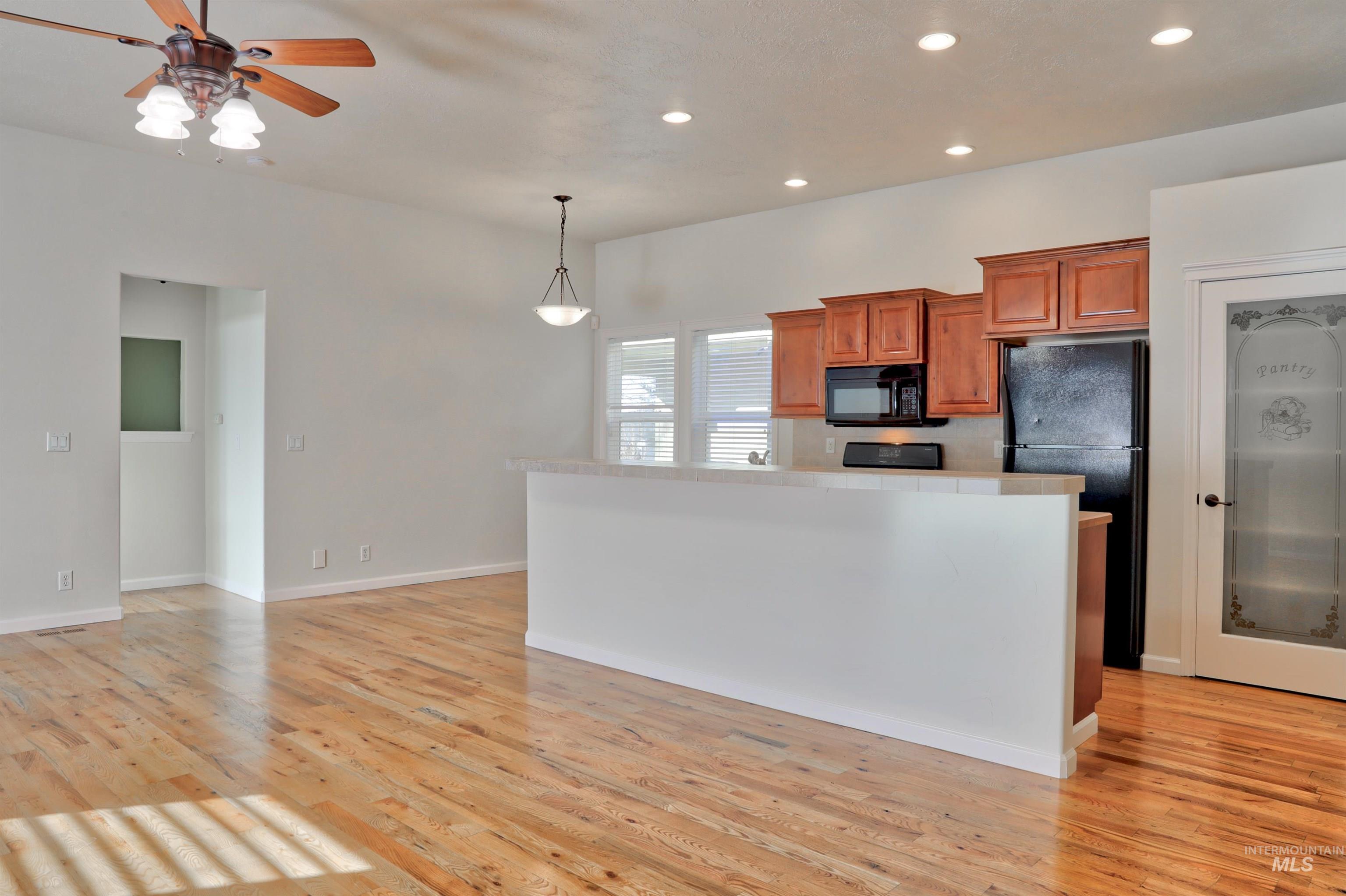 Kitchen featuring brown cabinets, decorative light fixtures, black appliances, recessed lighting, and a center island