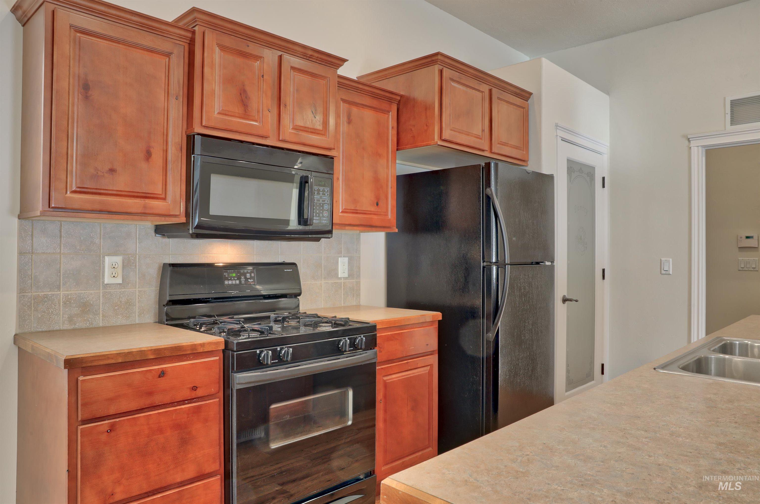 Kitchen featuring black appliances, light countertops, brown cabinets, and backsplash