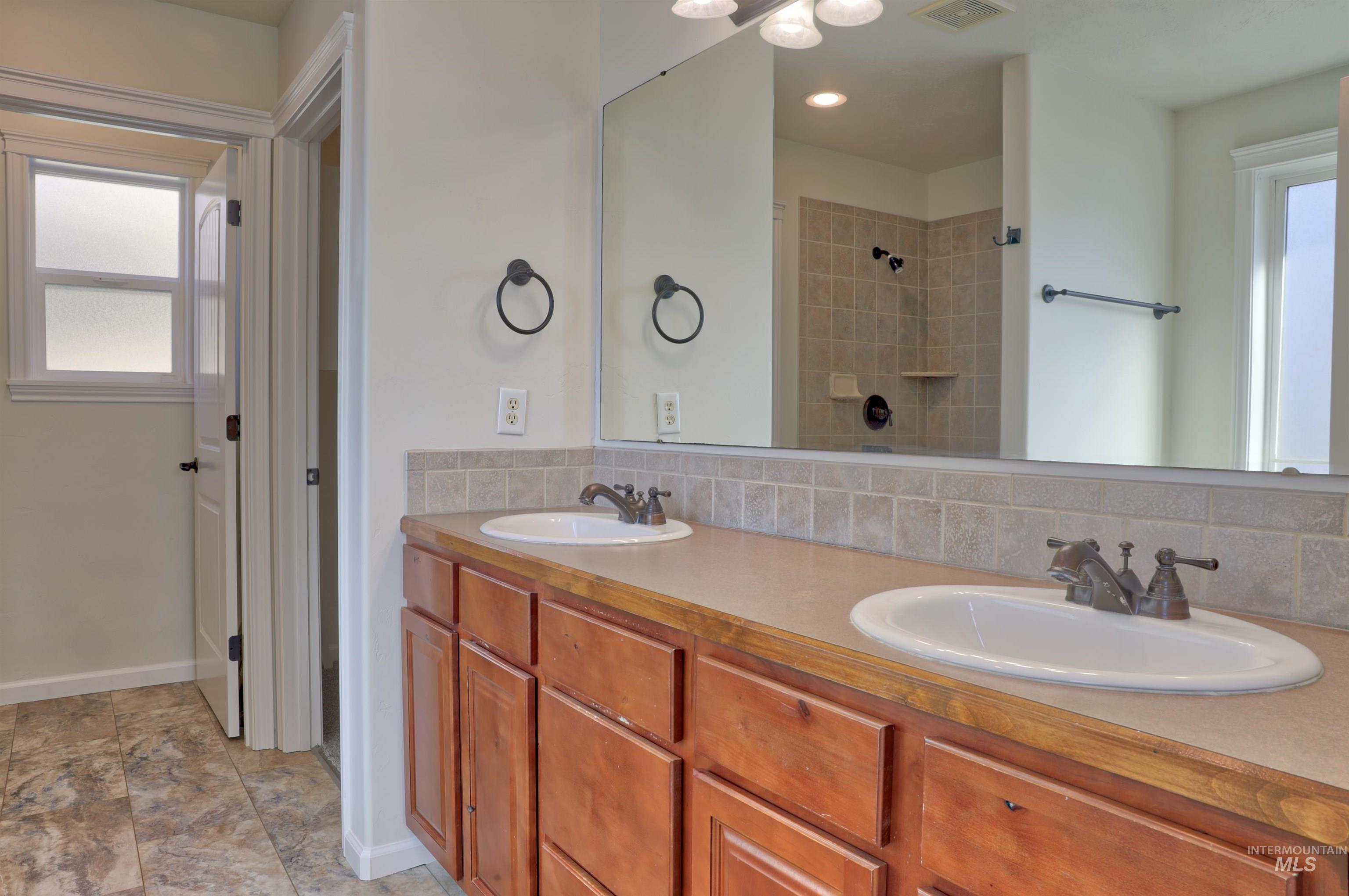 Full bath with plenty of natural light, double vanity, decorative backsplash, and tiled shower