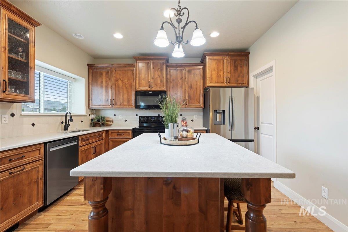 Kitchen featuring brown cabinetry, a center island, black appliances, and glass insert cabinets