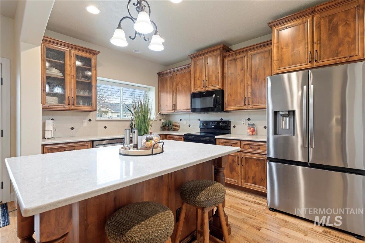 Kitchen with black appliances, a kitchen breakfast bar, brown cabinets, glass insert cabinets, and recessed lighting